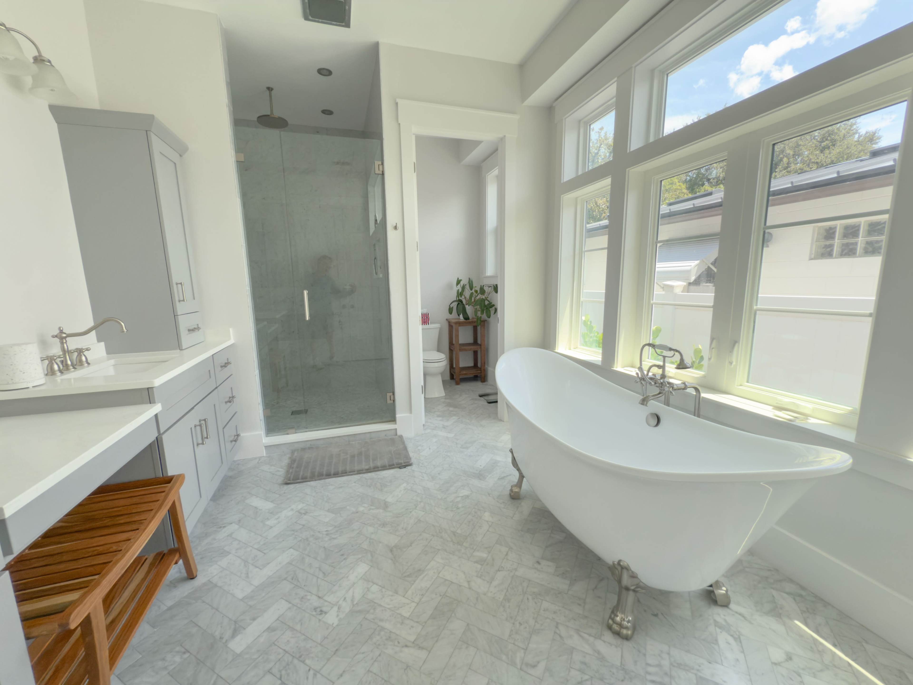 A spacious, modern bathroom features a freestanding bathtub, a glass shower, and large windows that provide natural light.