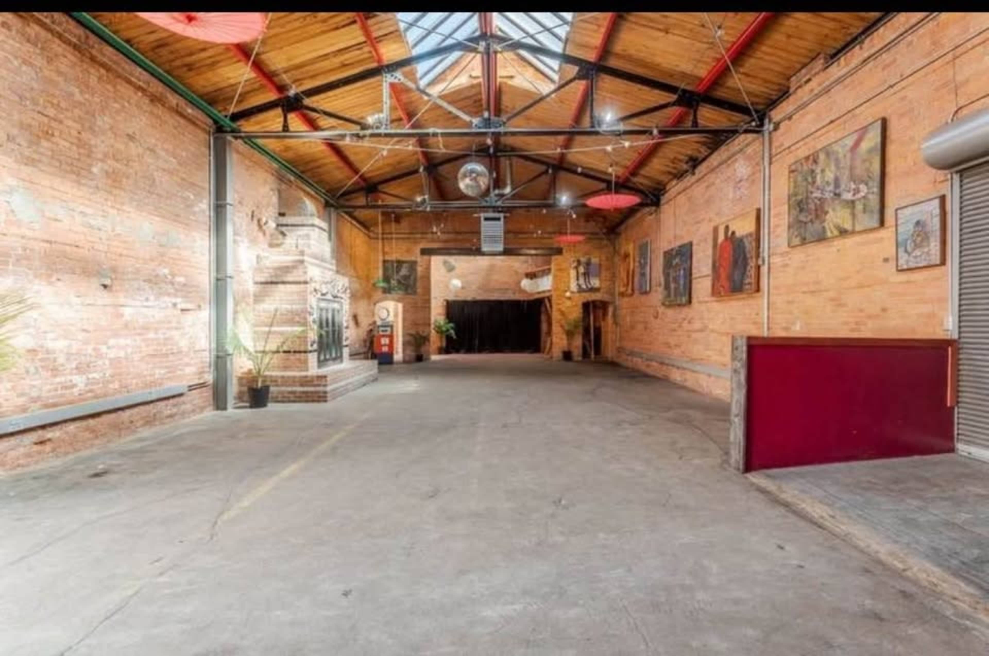 The image shows a spacious, industrial-style interior with brick walls, wooden beams, and various artworks hanging on the walls.