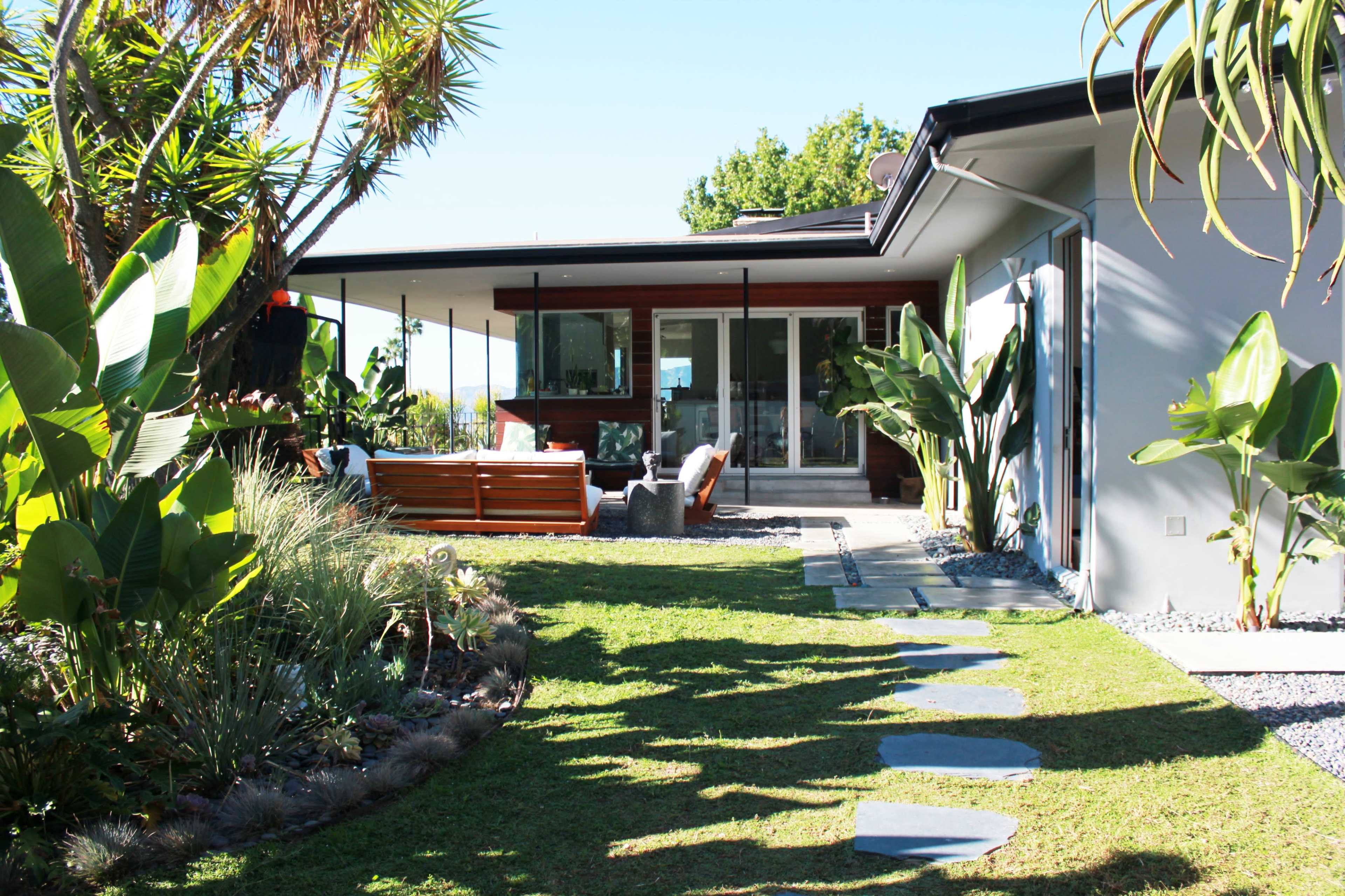 A pathway of stones leads through a landscaped yard to a modern house with large glass doors and a deck.