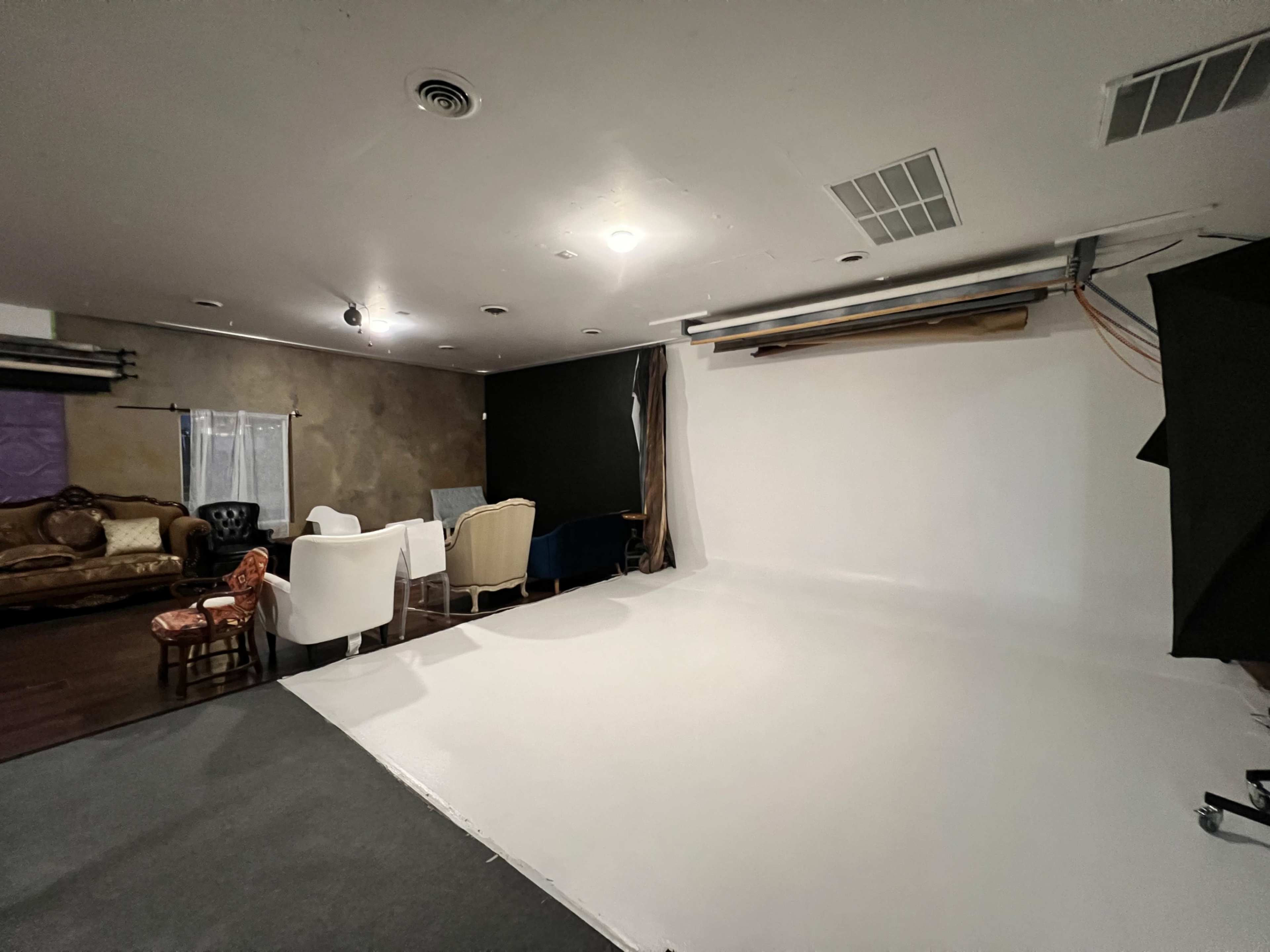 The image shows a partially set-up photography studio with a white backdrop and several chairs arranged around the space, along with a couch in the corner.