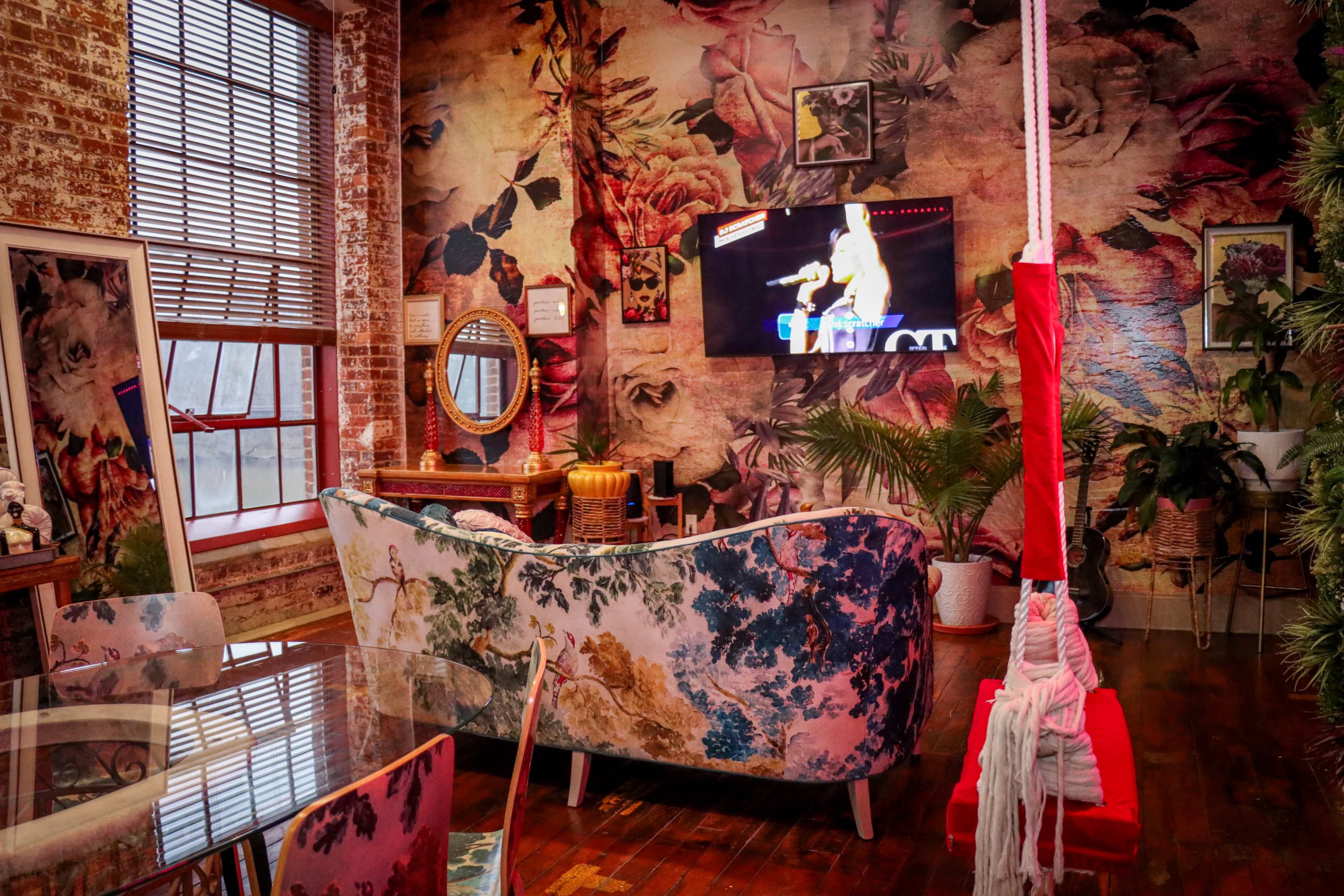 A colorful living room with floral wallpaper, a television displaying a performance, and a swing hanging from the ceiling.