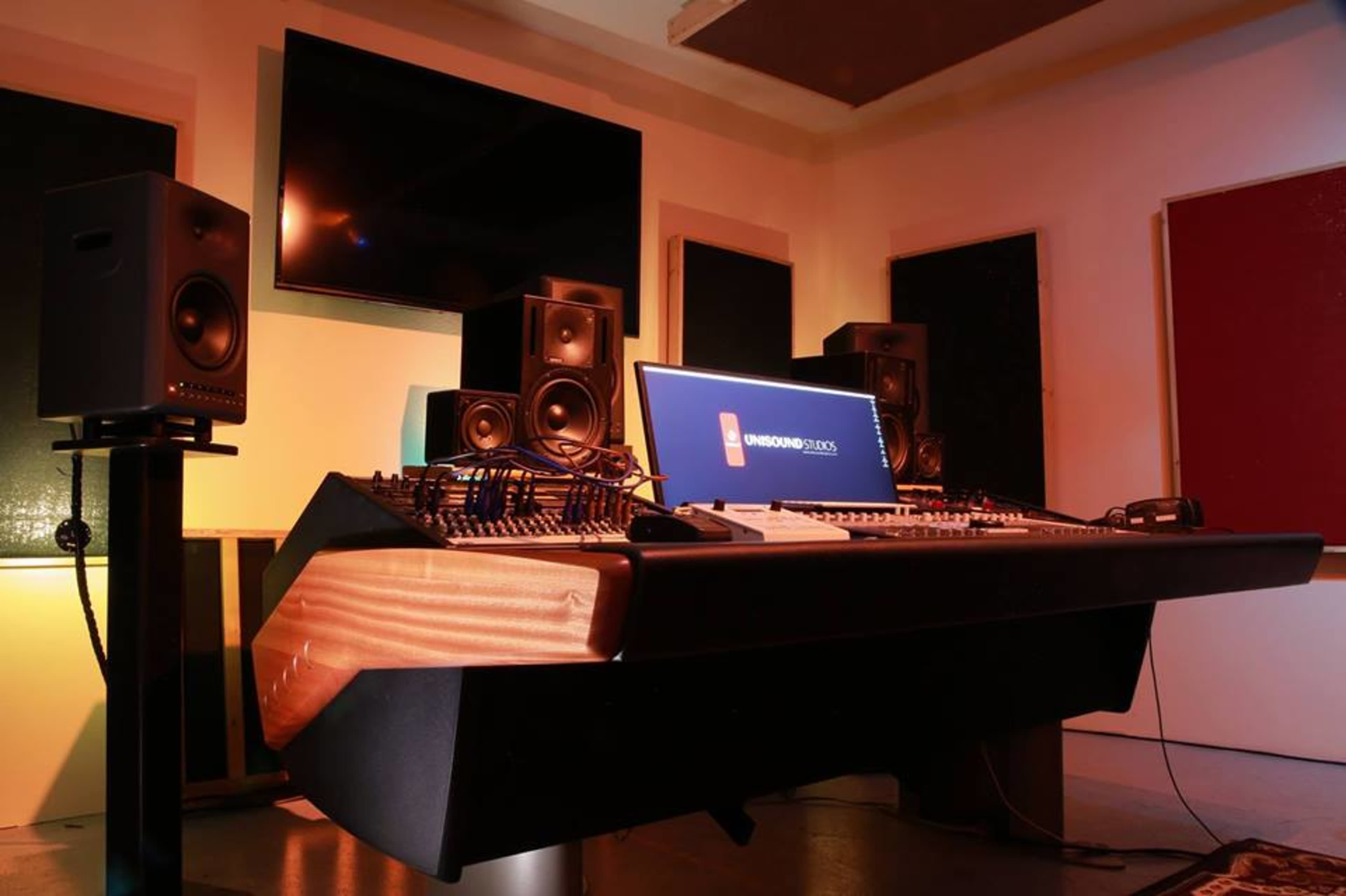 A music production studio featuring a mixing console, studio monitors, and a large screen displaying the "Soundproof Studios" logo.