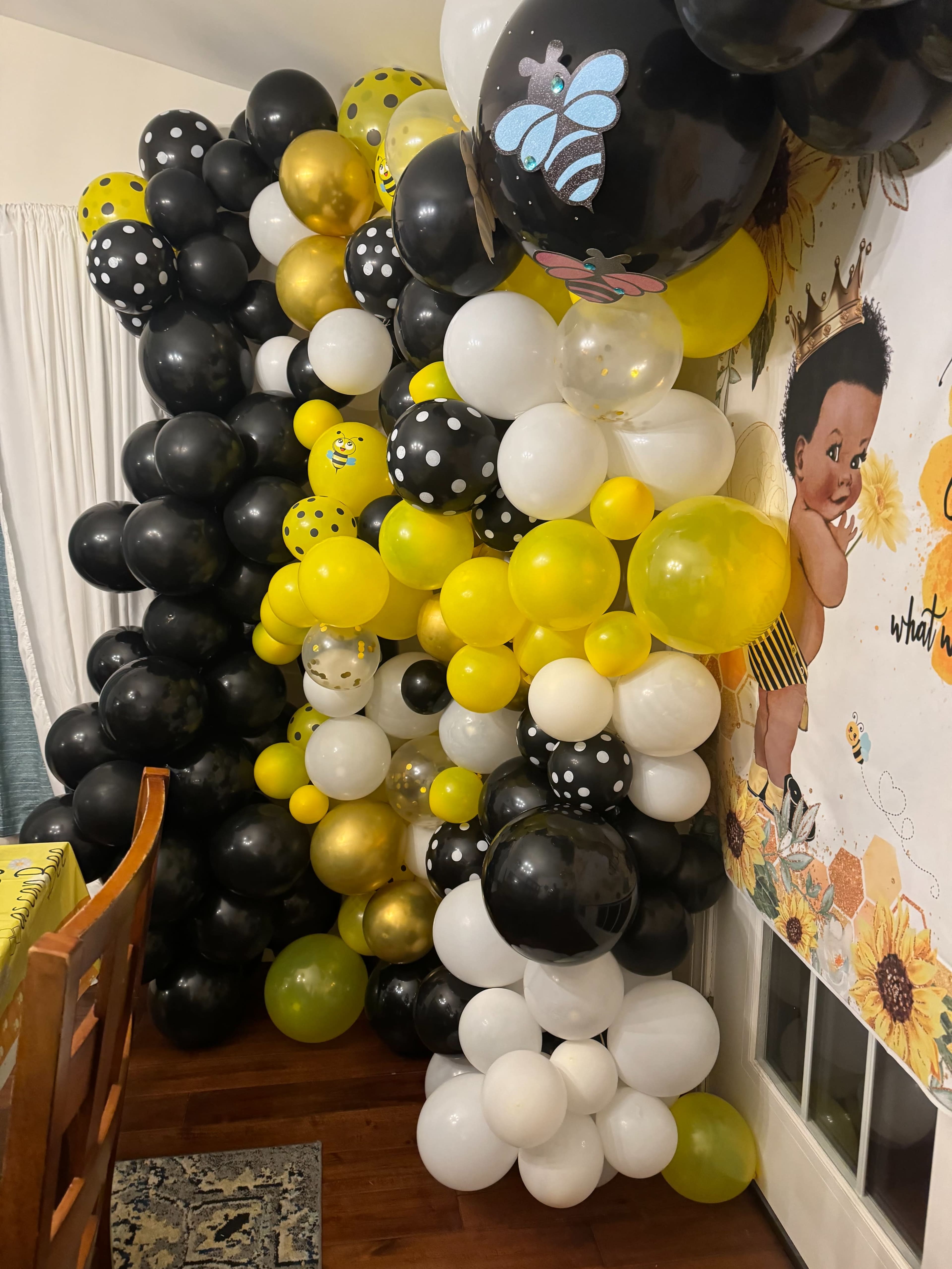 A decorative wall of balloons in black, white, and yellow clusters is arranged next to a wall featuring a cartoonish character.