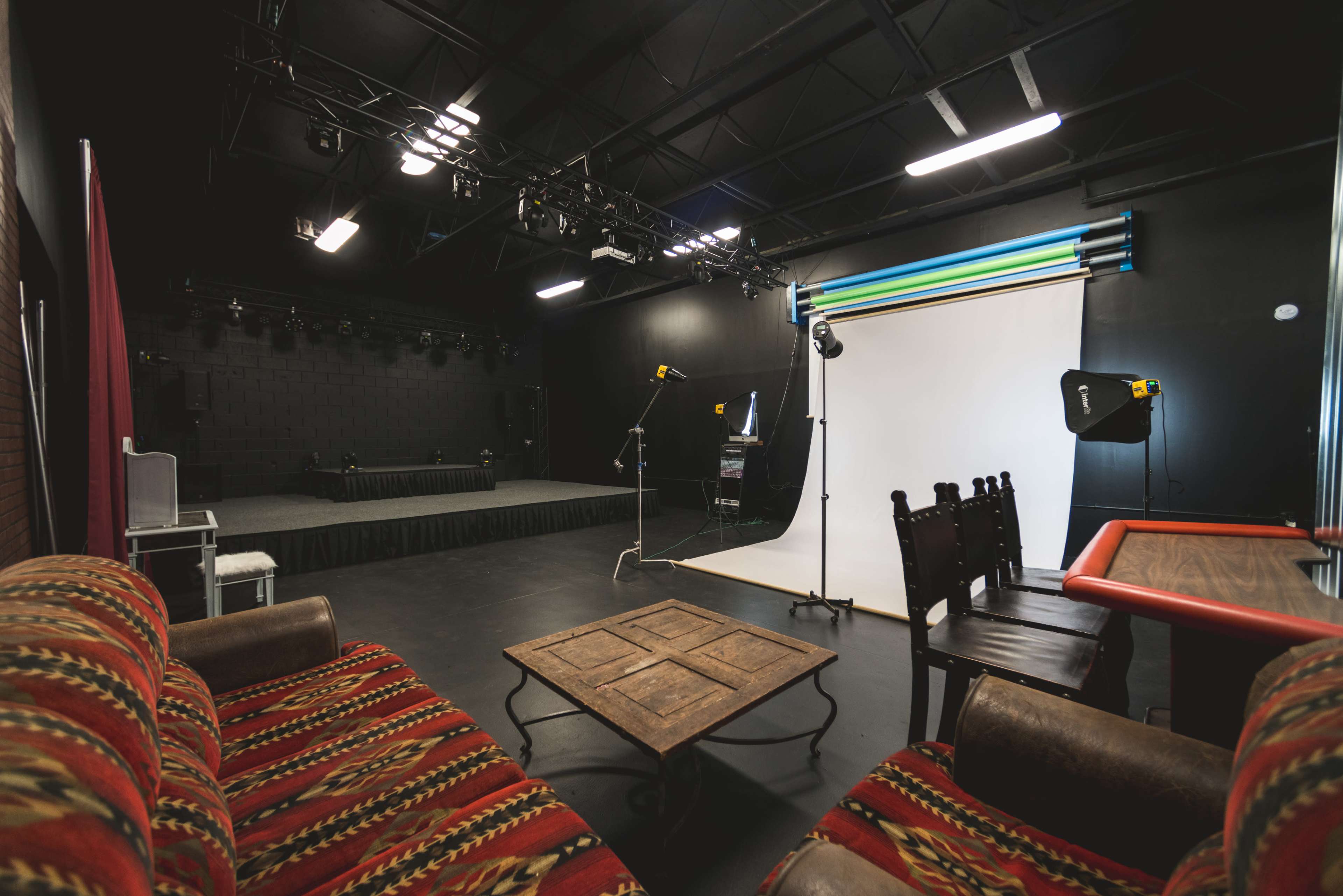 A photography studio featuring a large backdrop, lighting equipment, a wooden table, and a patterned sofa.