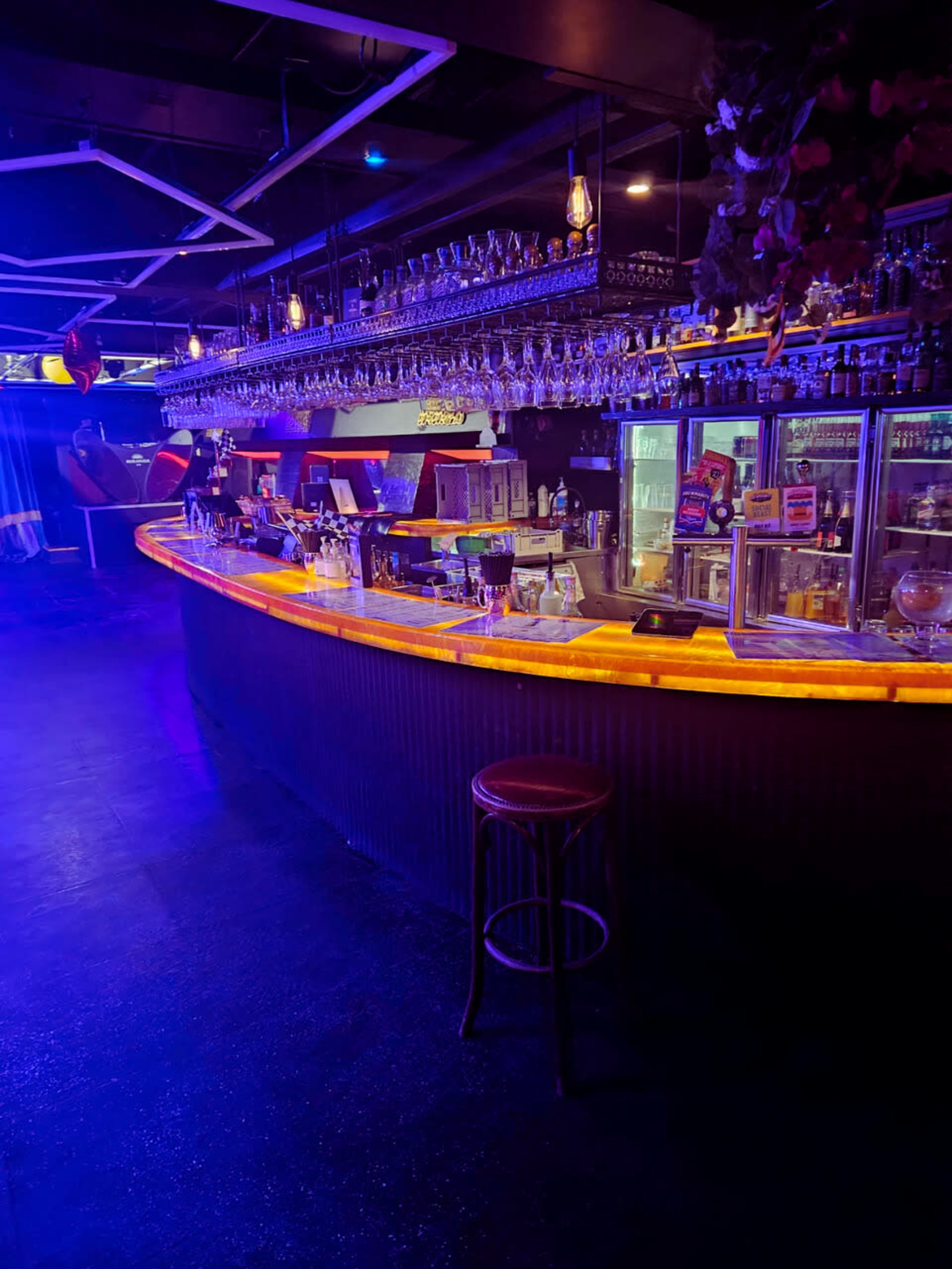 The scene shows a dimly lit bar with a curved counter illuminated by a vibrant orange light and shelves lined with glassware.