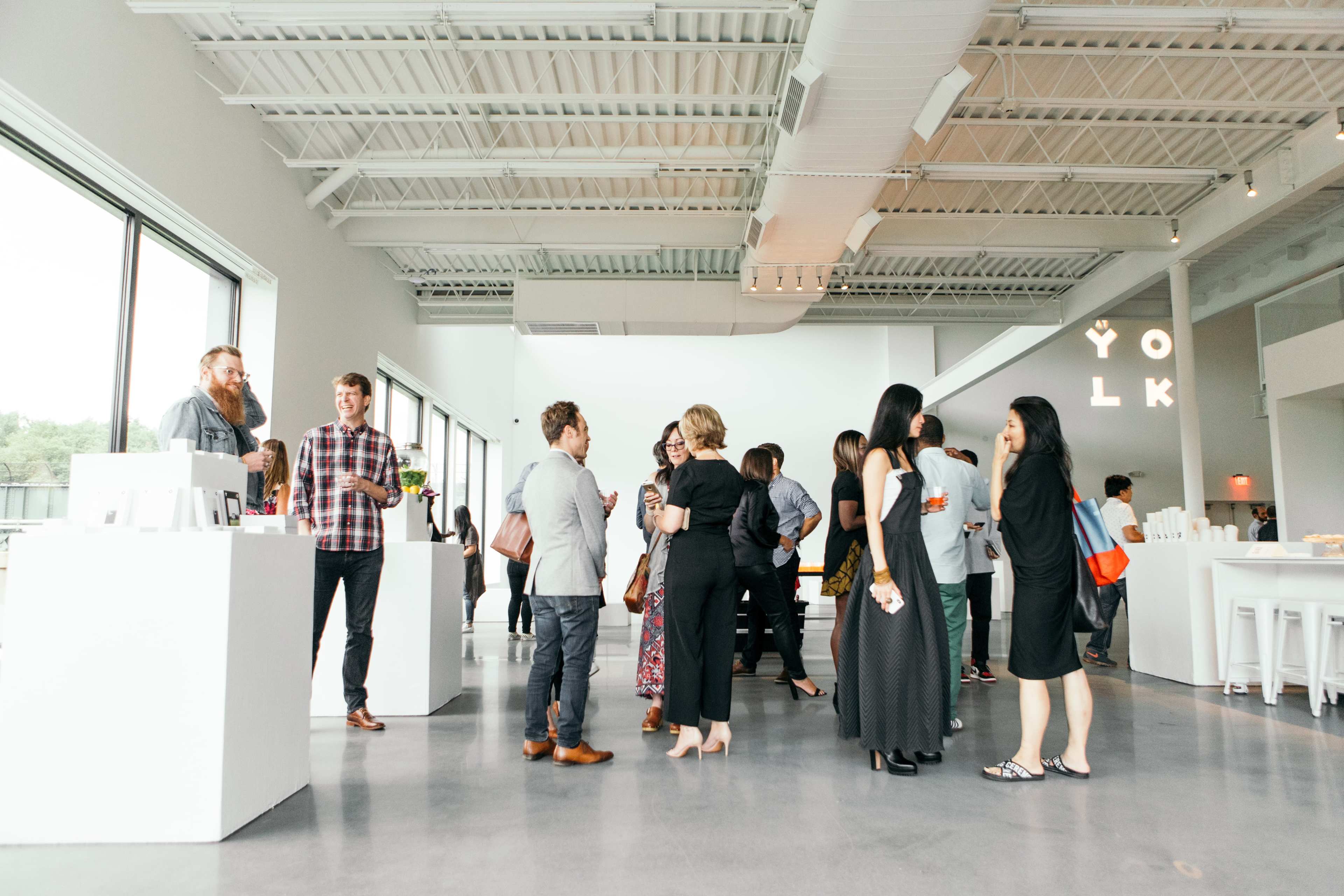 A group of people mingles at a modern event space with large windows and minimalist decor.