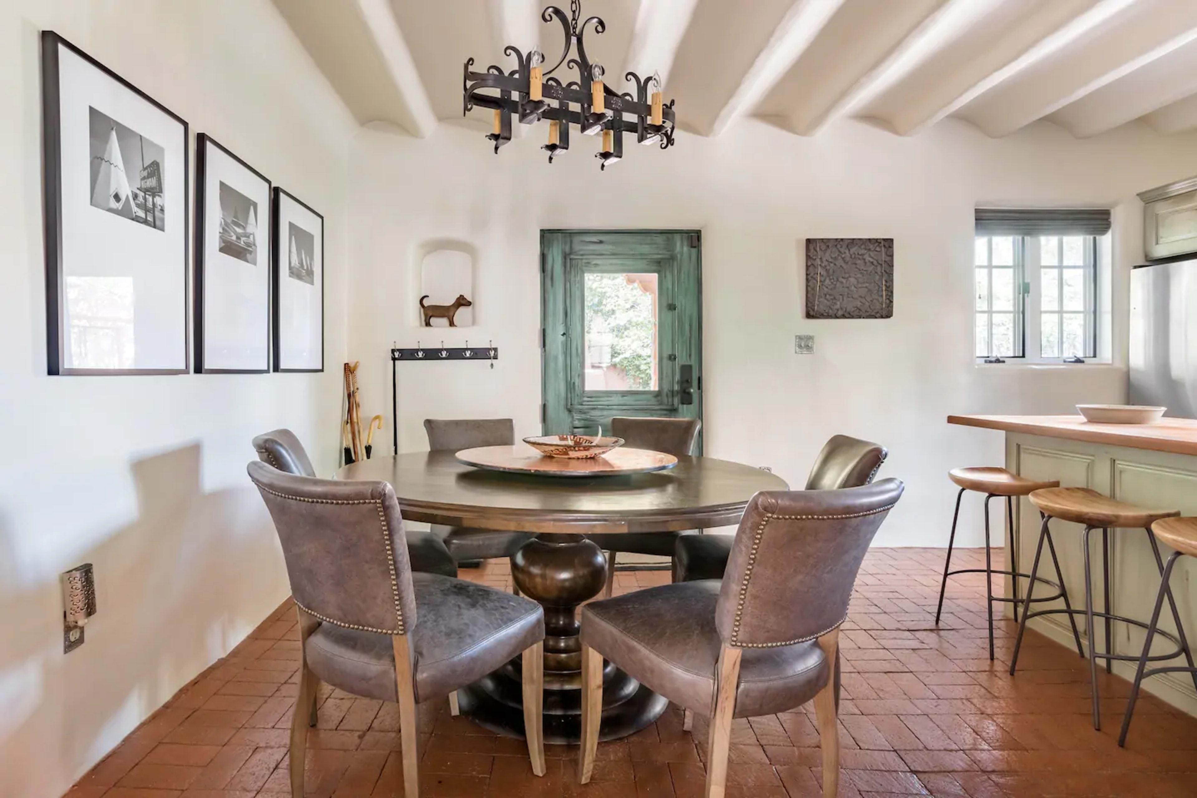 A round dining table surrounded by four upholstered chairs is set in a brightly lit room with white walls and a wooden ceiling.