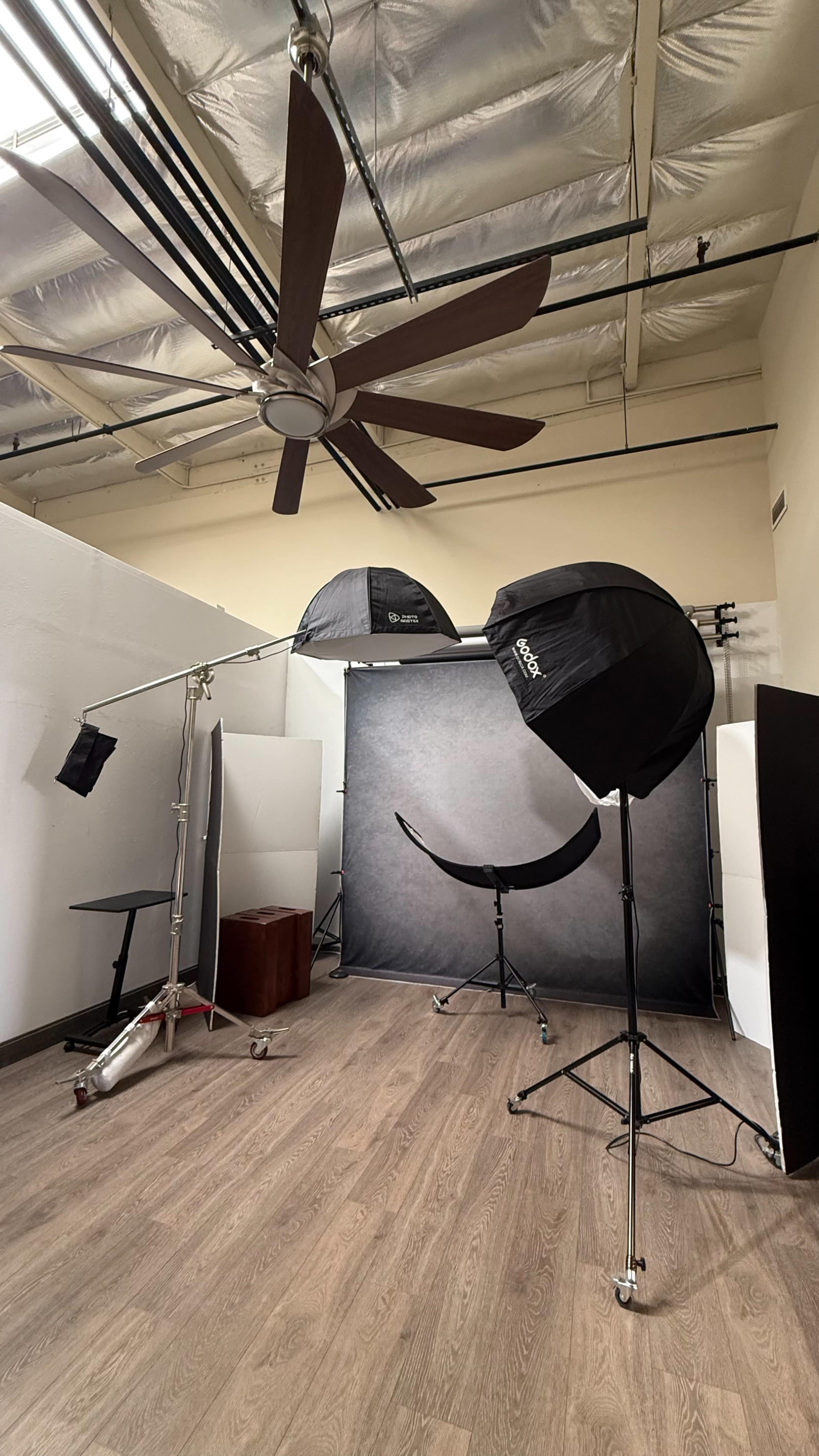 The image shows a photography studio equipped with softbox lights, a backdrop, and studio accessories set up on wooden flooring.