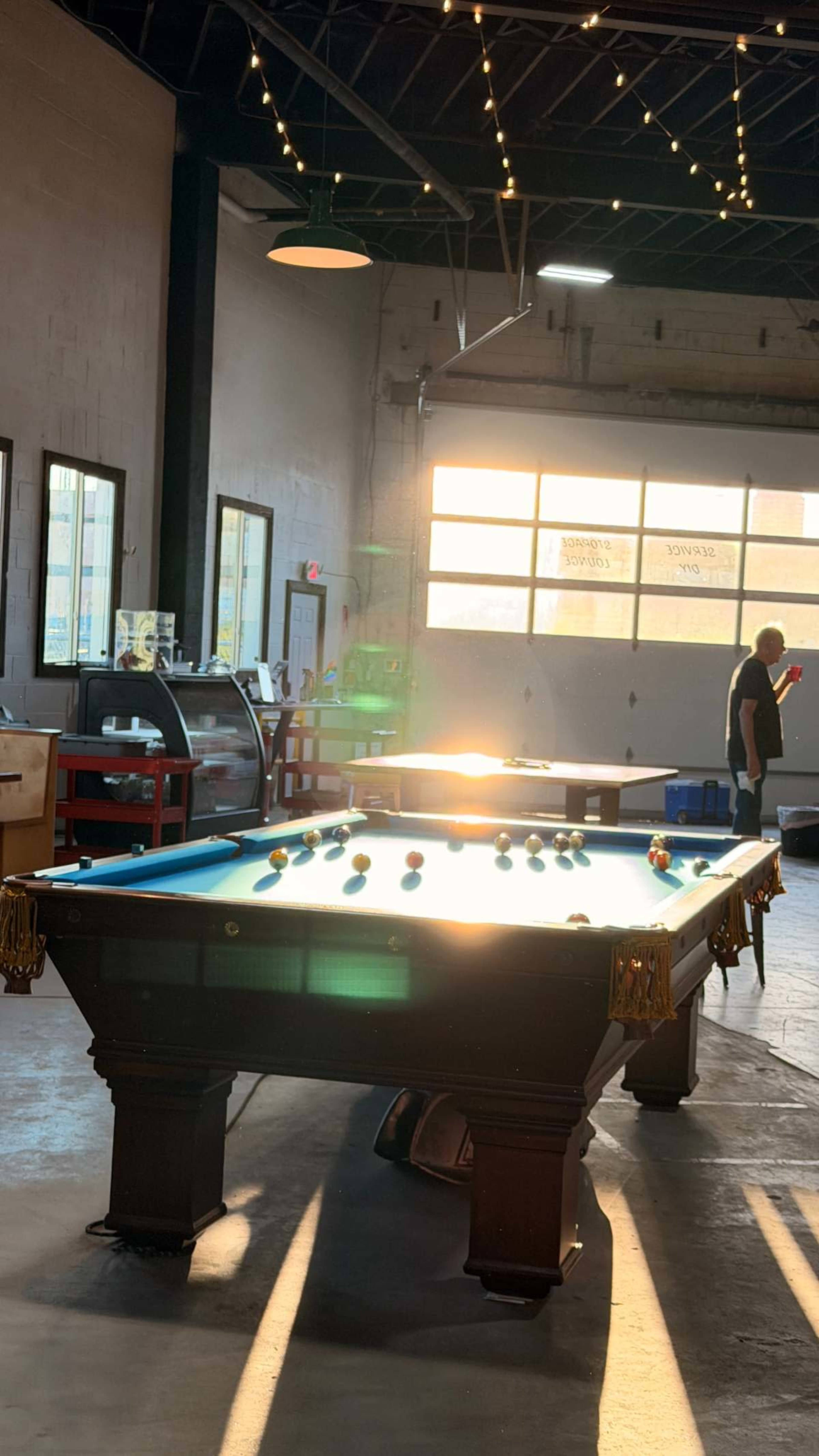 A billiard table is illuminated by sunlight in a spacious recreational room with large windows.