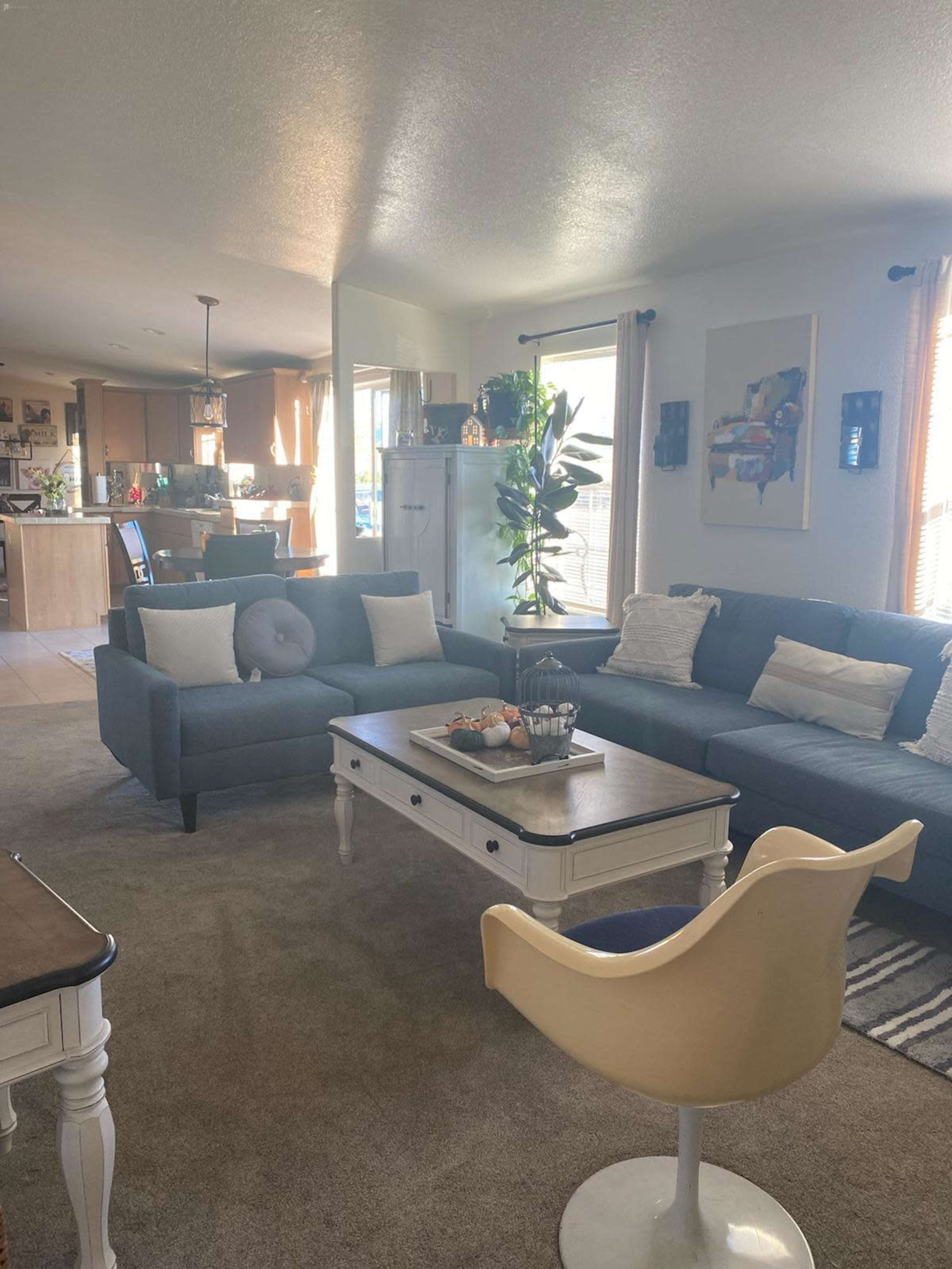 A living room with a blue sofa, a coffee table, and a dining area visible in the background.