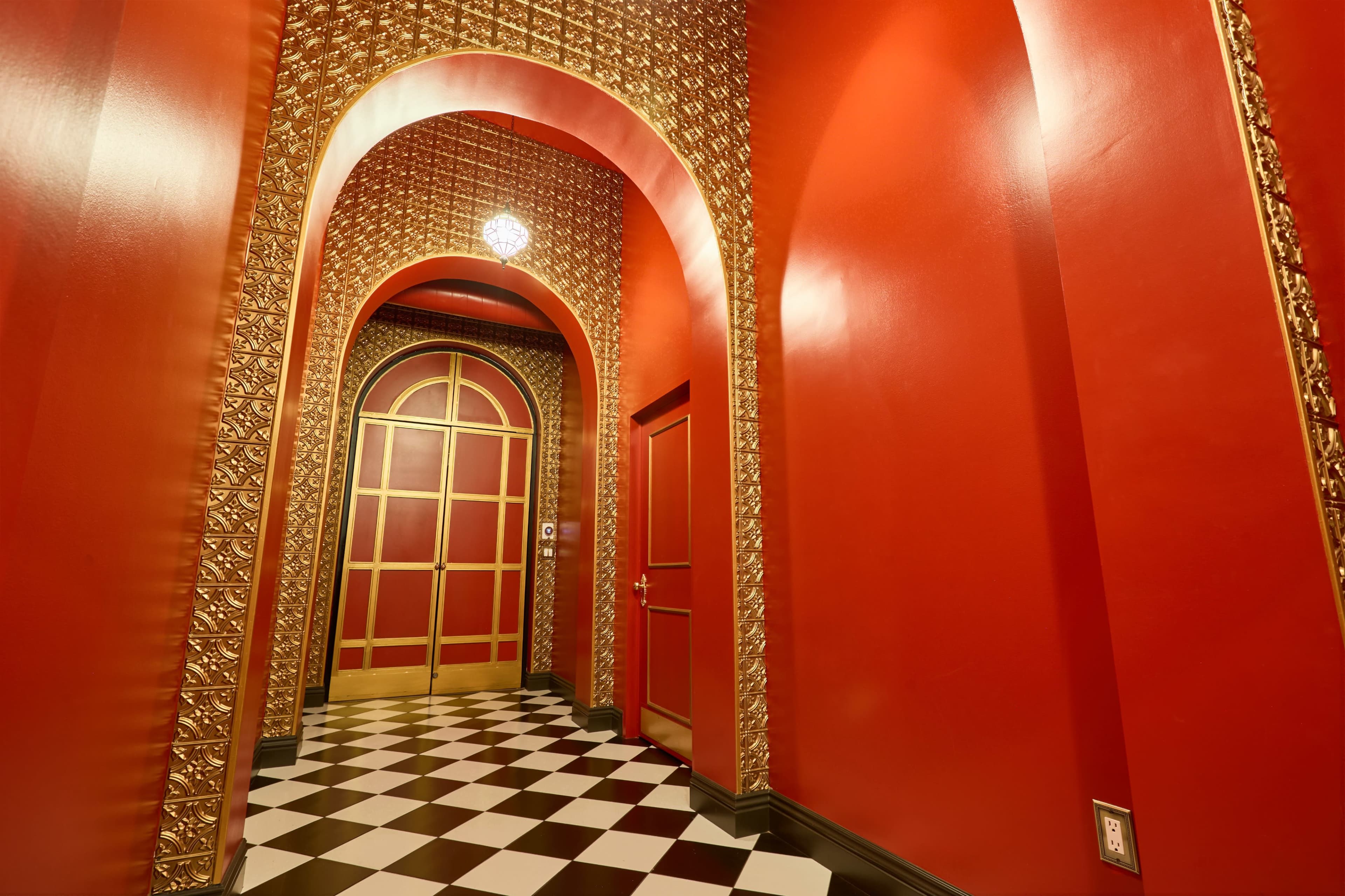 The image shows a hallway with red walls adorned with gold detailing and a checkered black and white floor.