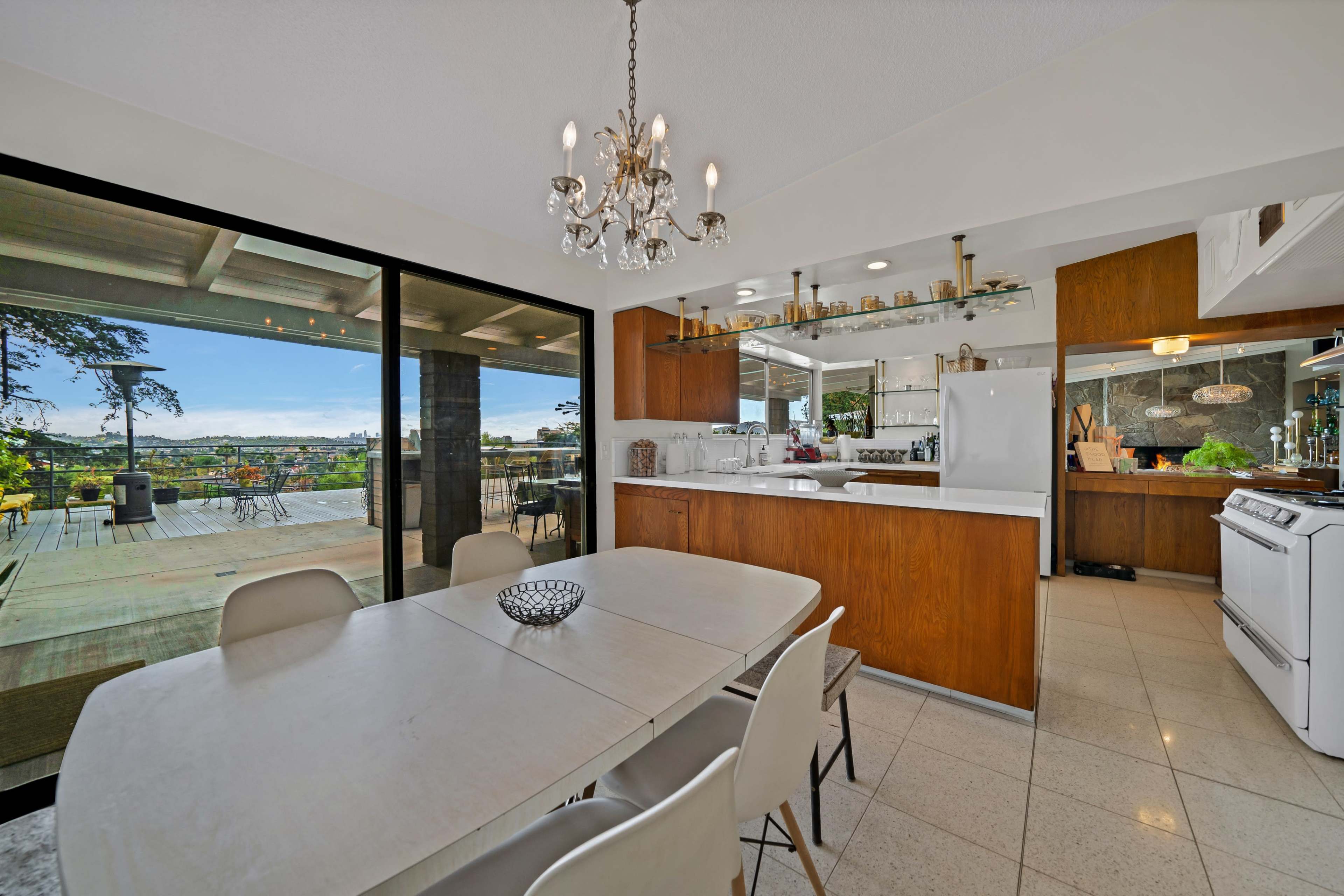 The image shows a modern dining area with a chandelier, a large table, and a view of an outdoor patio through floor-to-ceiling sliding glass doors.