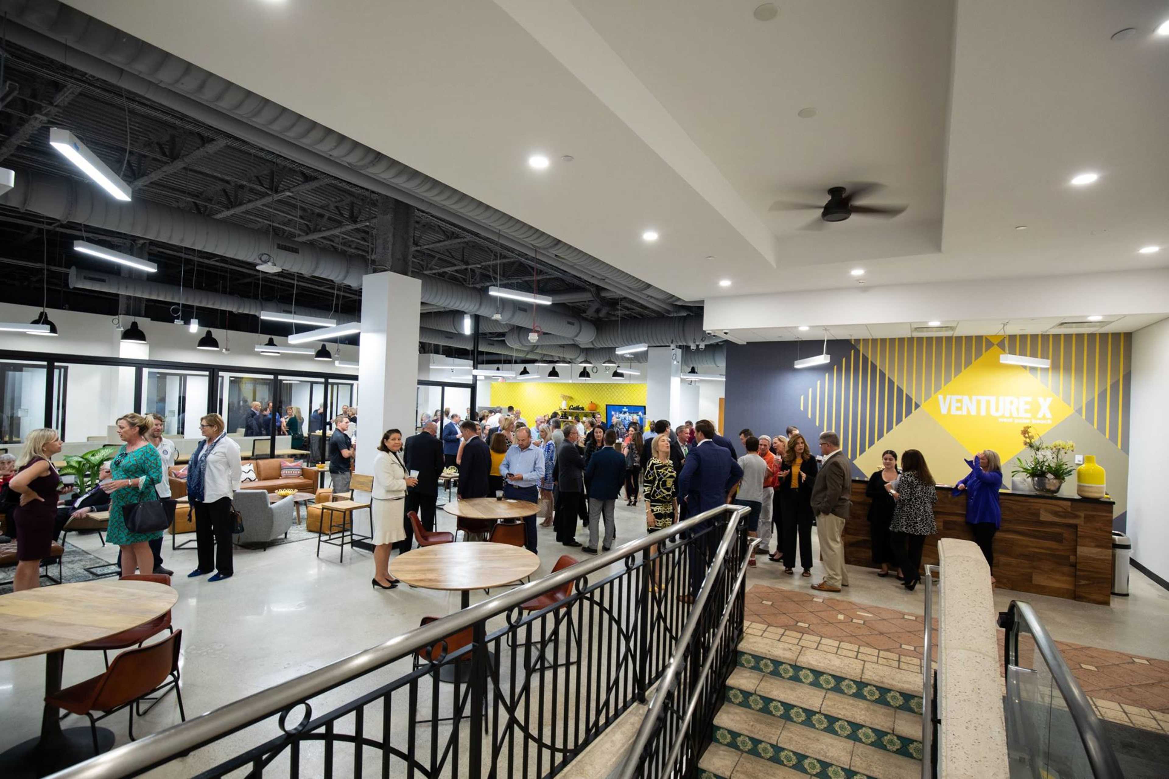 A large group of people gathers in a modern open space with tables and a vibrant wall featuring the text "VENTURE X."