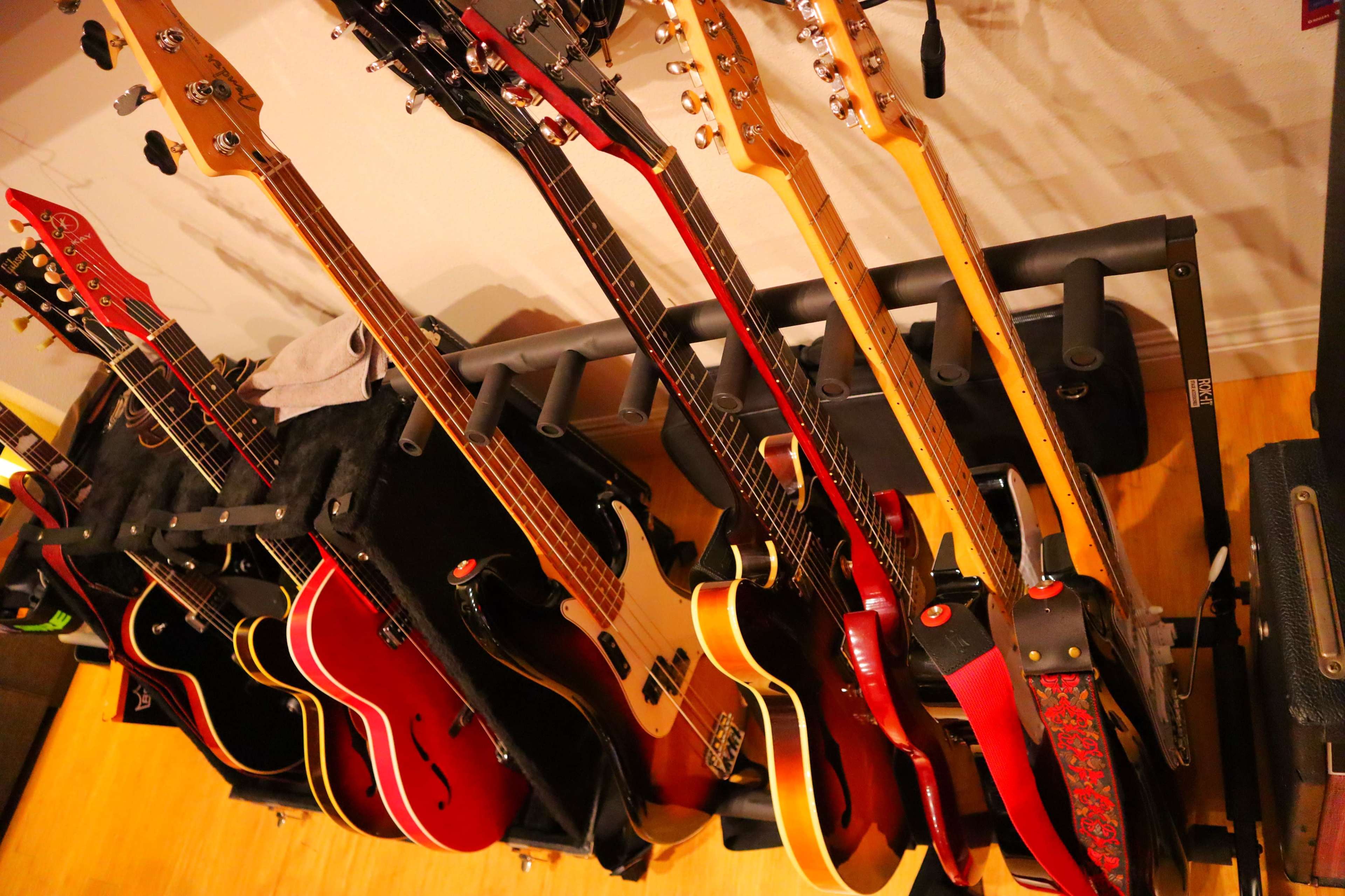 A row of various guitars and basses is displayed on a rack against a wall in a music room.