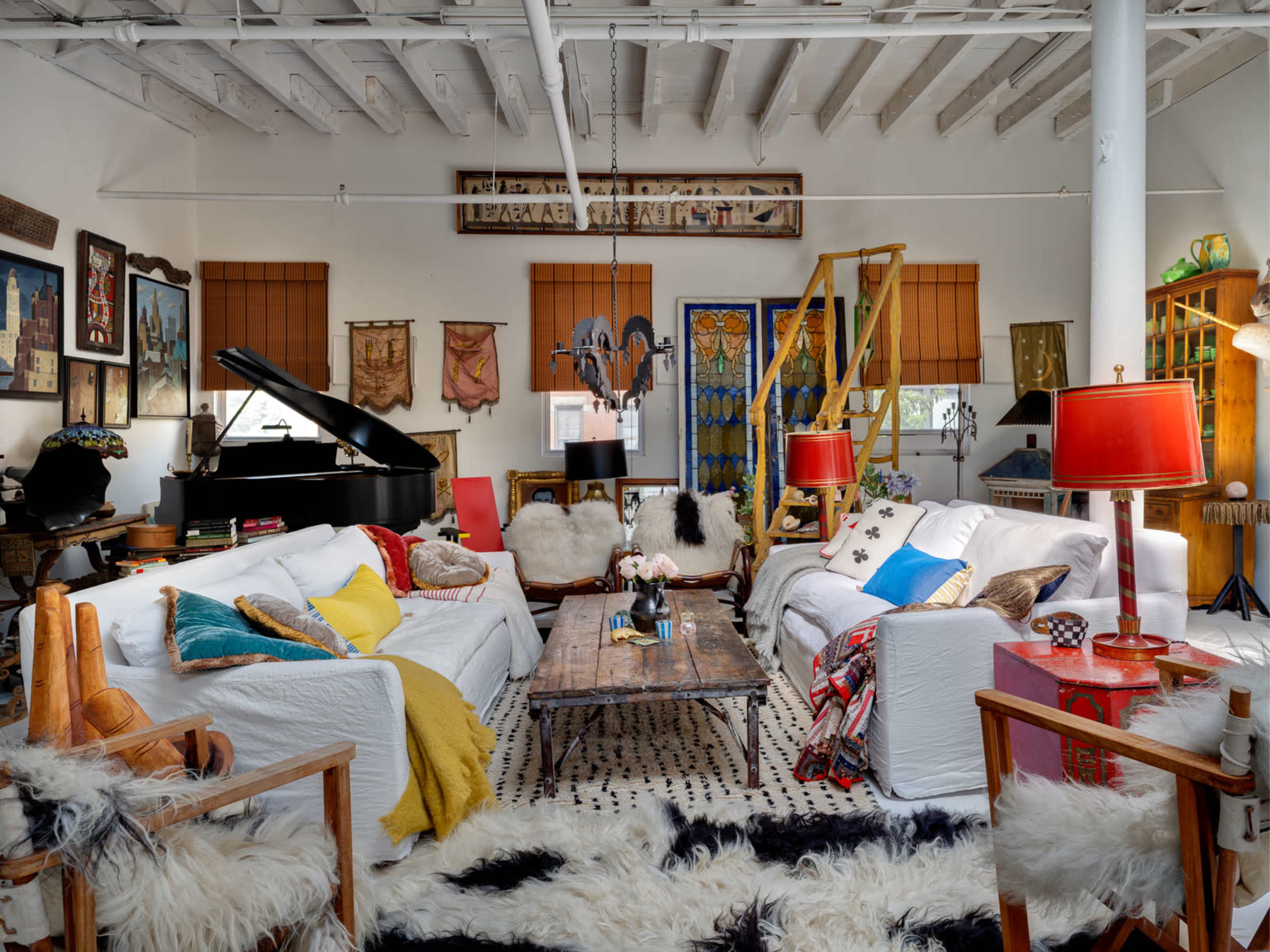 The image depicts a spacious living room featuring a piano, multiple sofas, a wooden coffee table, and decorative artwork on the walls.