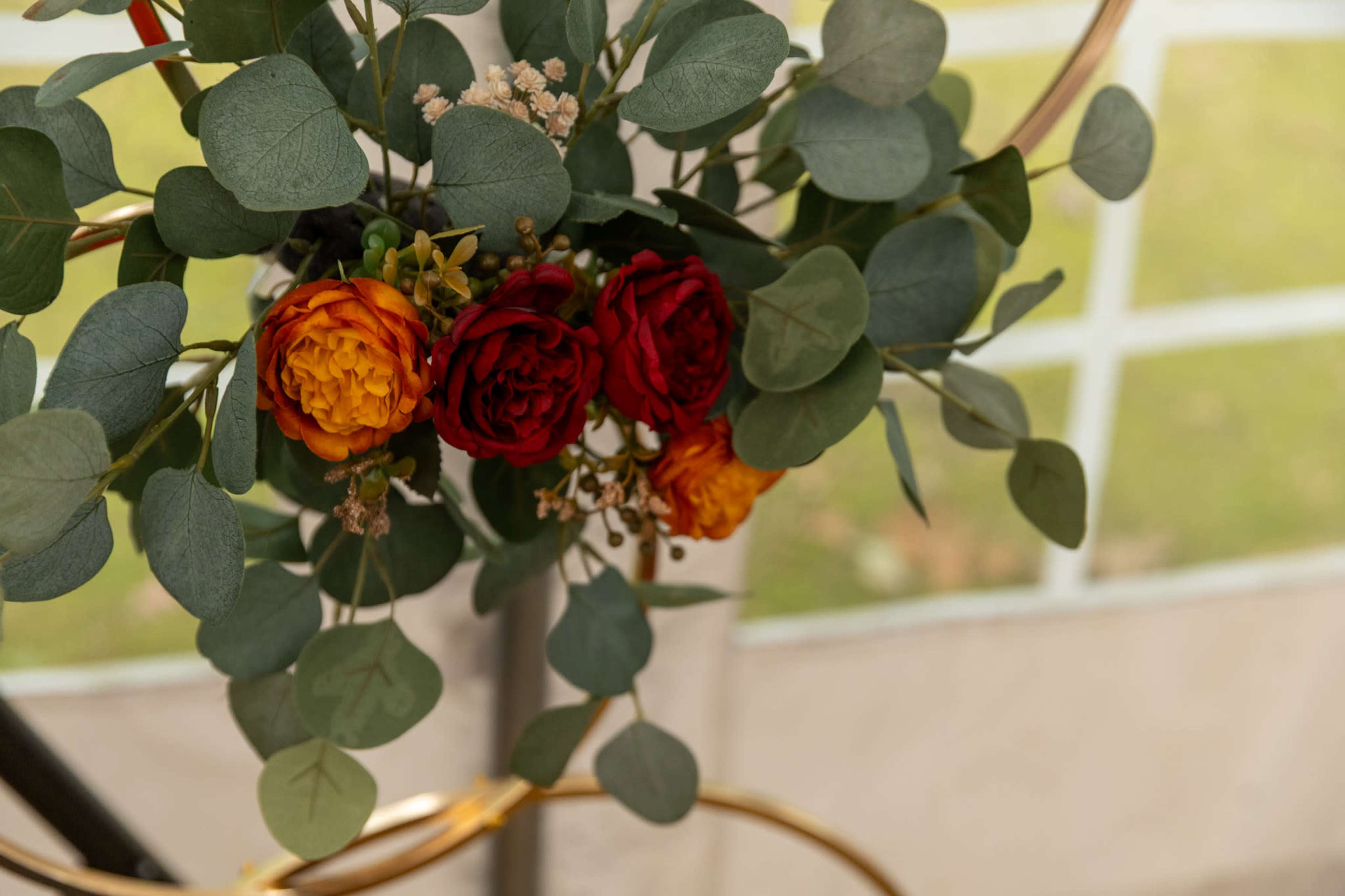 A floral arrangement featuring red and orange roses with greenery is displayed against a backdrop of a tent.