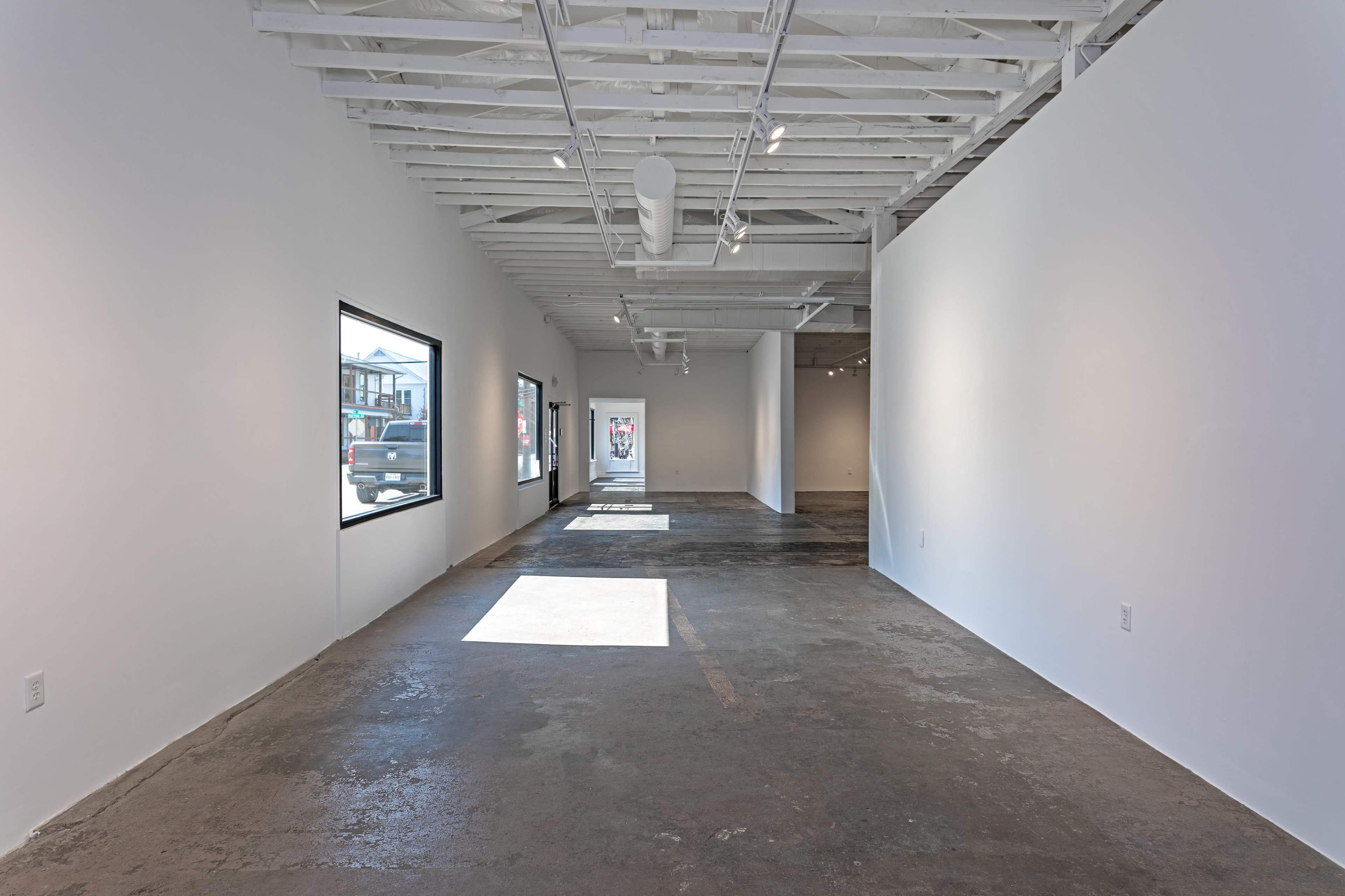 A spacious, empty art gallery with large windows and polished concrete floors.