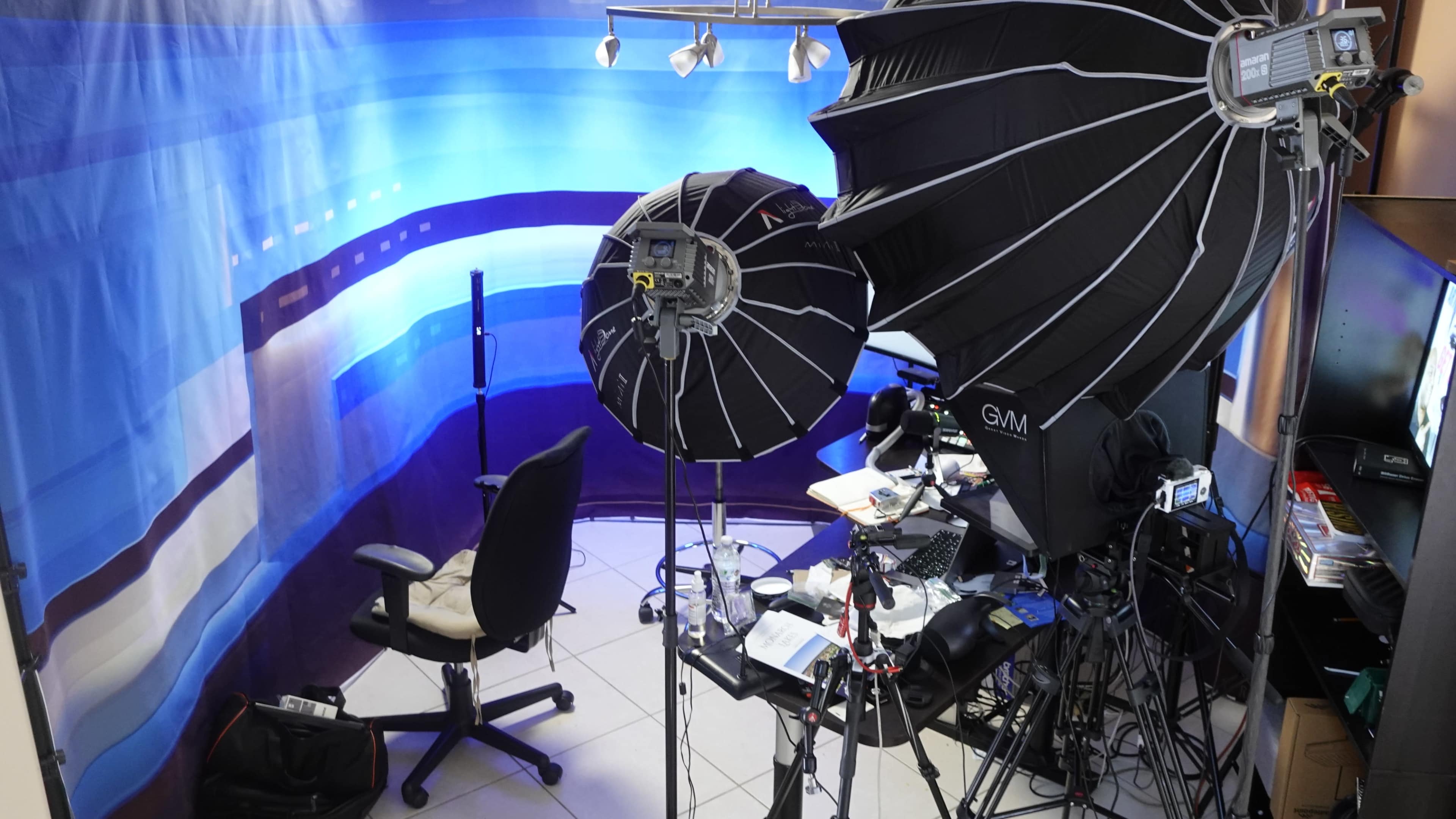 The image shows a photography setup with two large softbox lights, a chair, and various equipment in a studio space.