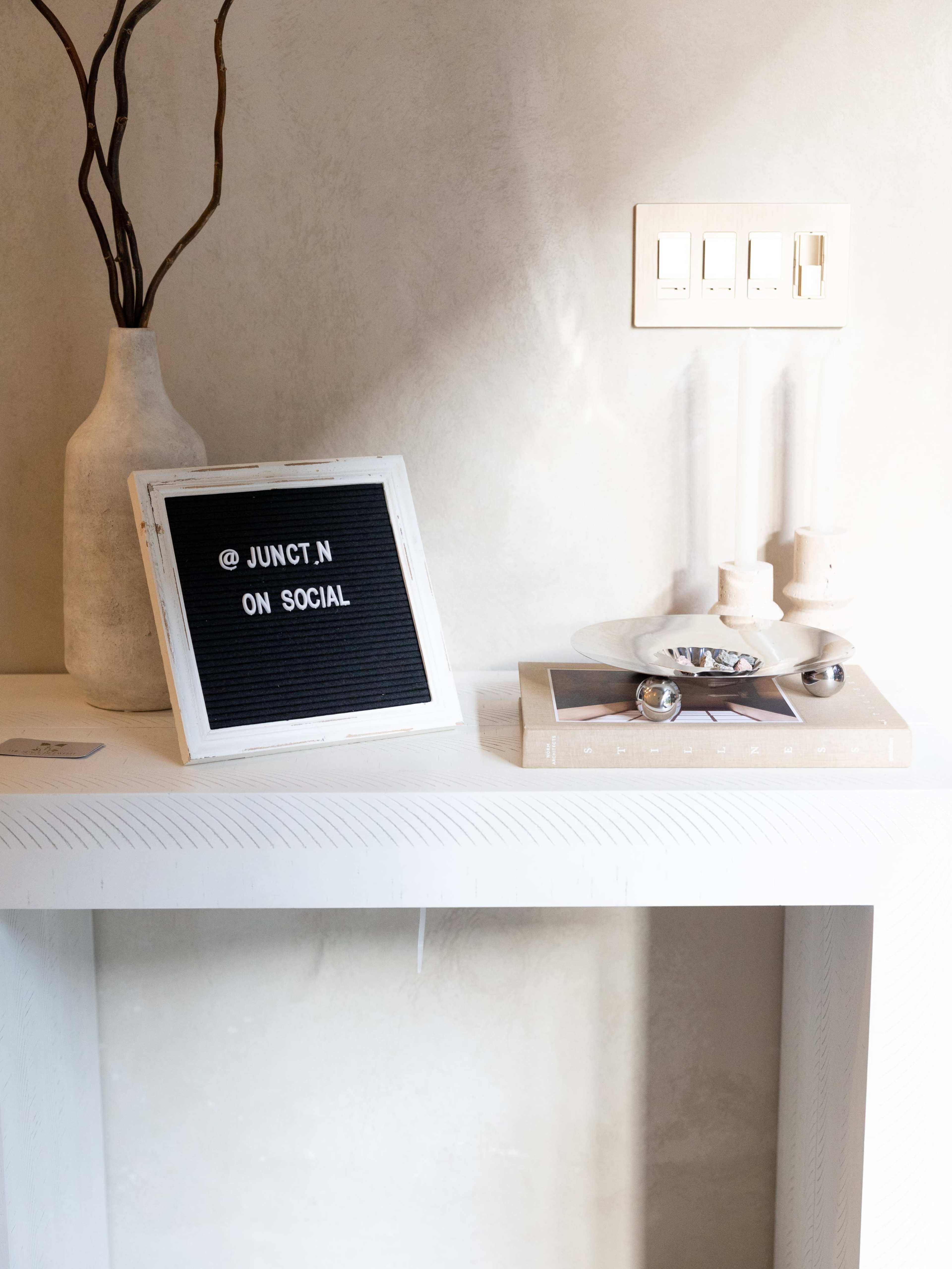 A white shelf displays a letter board with the text "@ JUNCT N ON SOCIAL," alongside a white vase and decorative items.