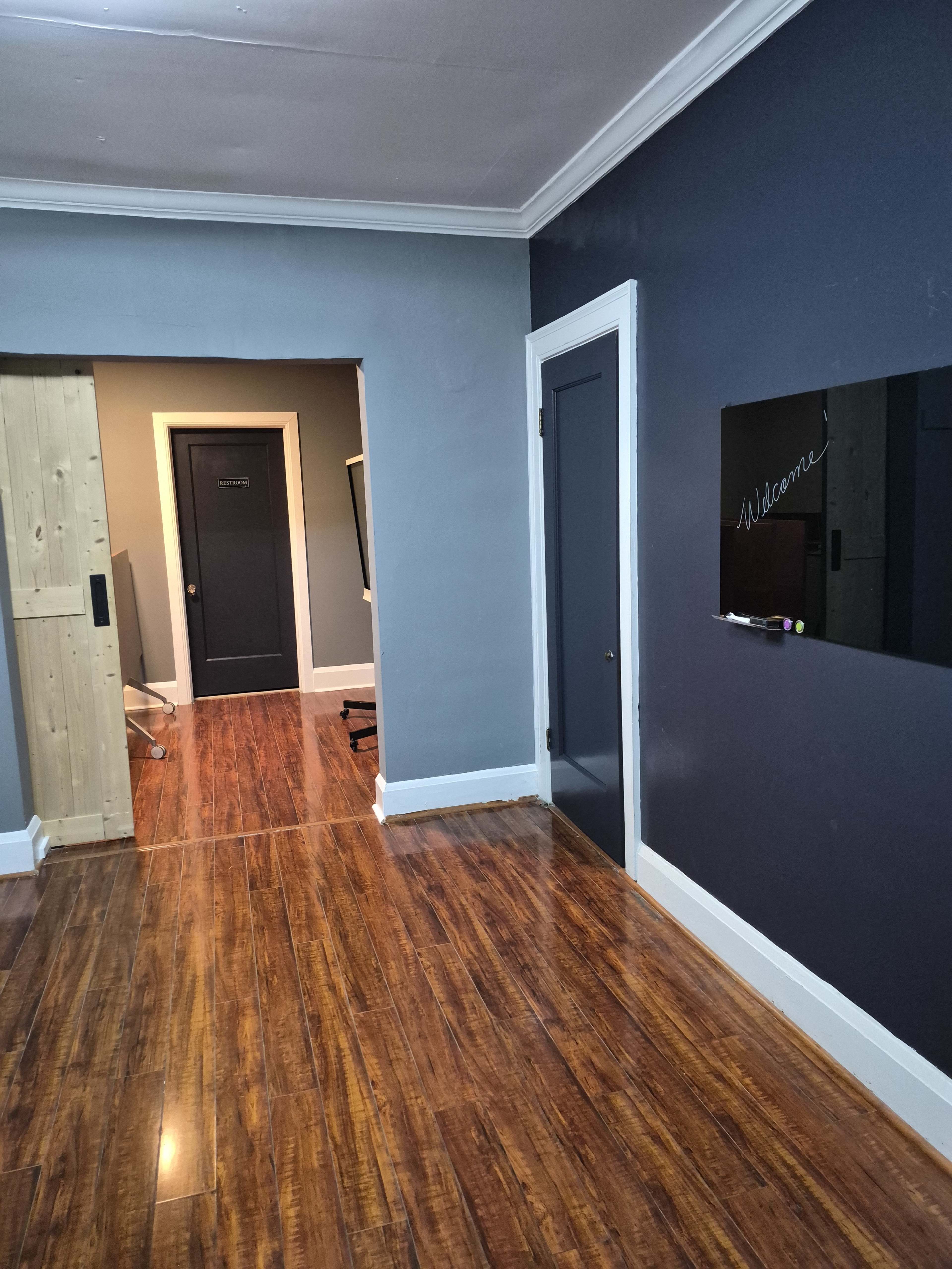 The image shows an interior space with wooden flooring, a dark gray wall, and two doorways leading to different rooms.
