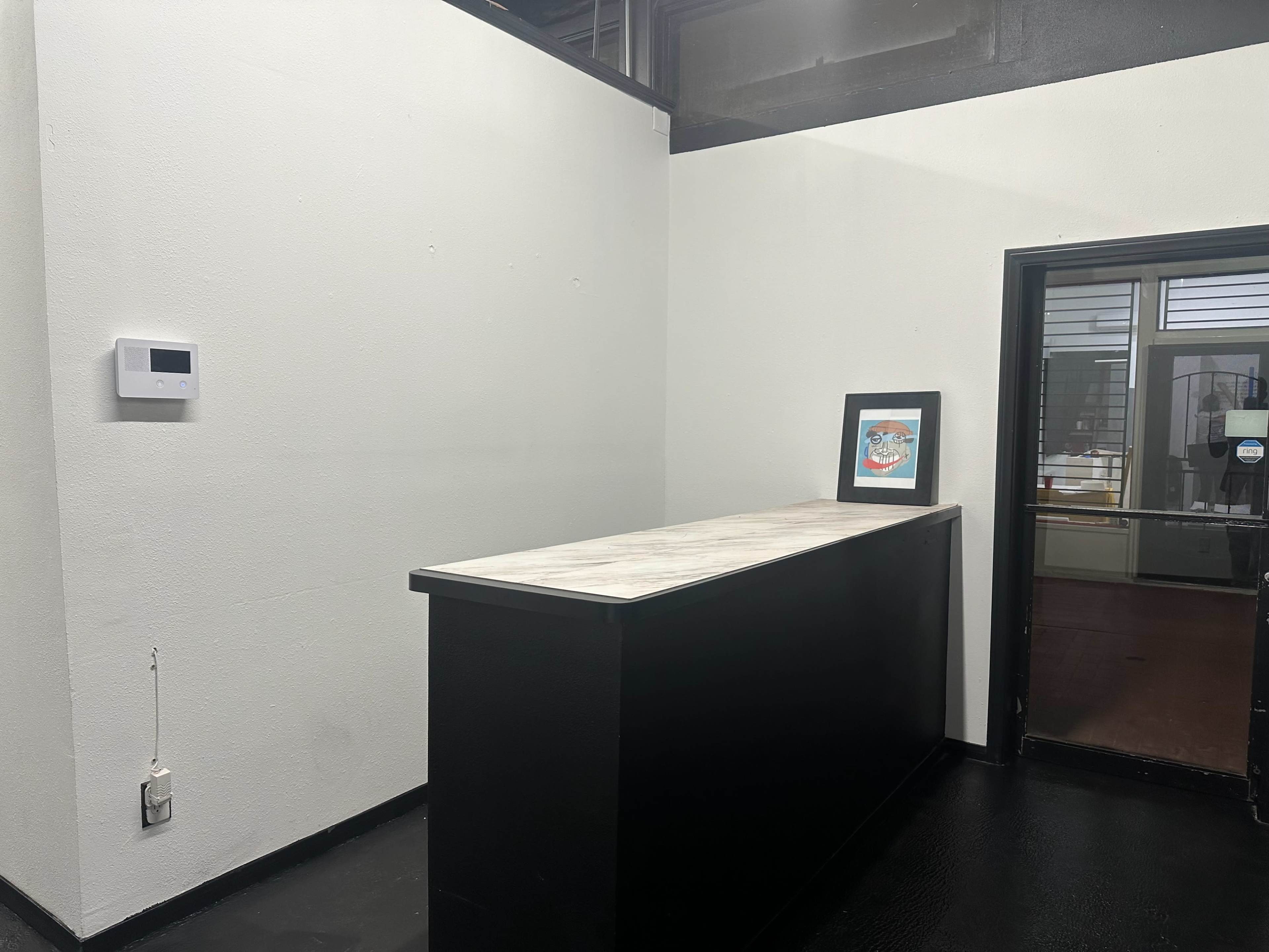A minimalist reception area with a black counter and a framed artwork on top, against a white wall.