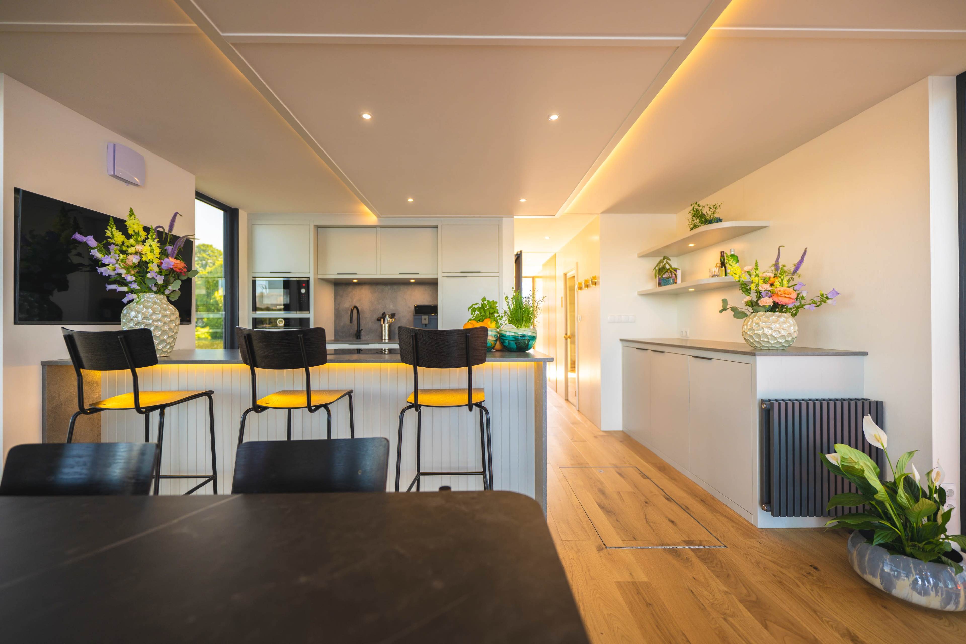 A modern kitchen features a central island with four black stools and bright yellow cushions, alongside sleek cabinetry and natural light from large windows.