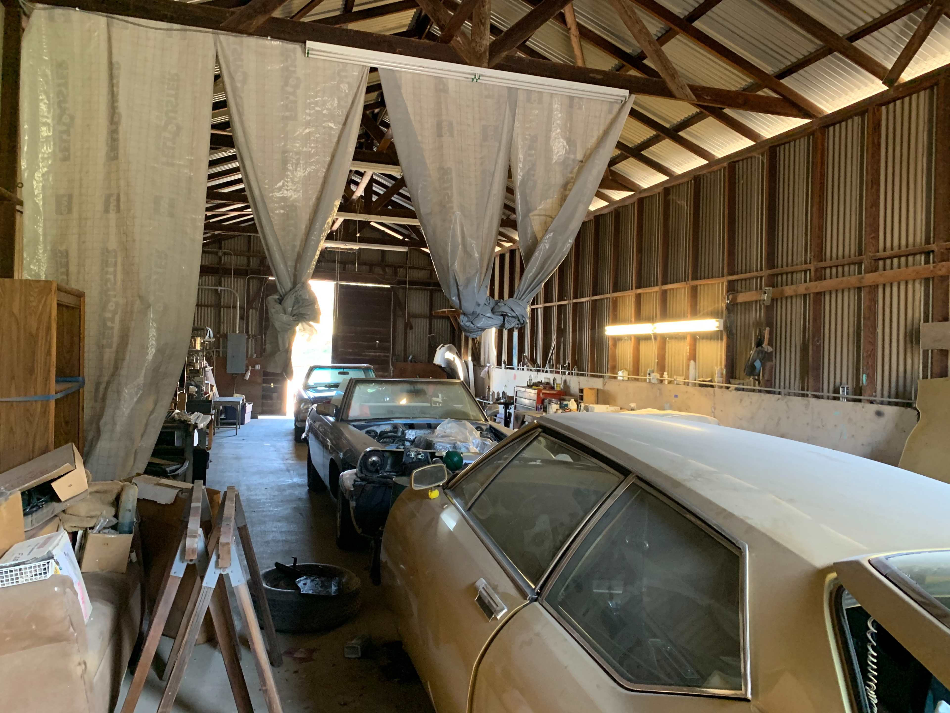A spacious garage with two vintage cars parked on the right and a set of curtains partially blocking the entrance at the far end.