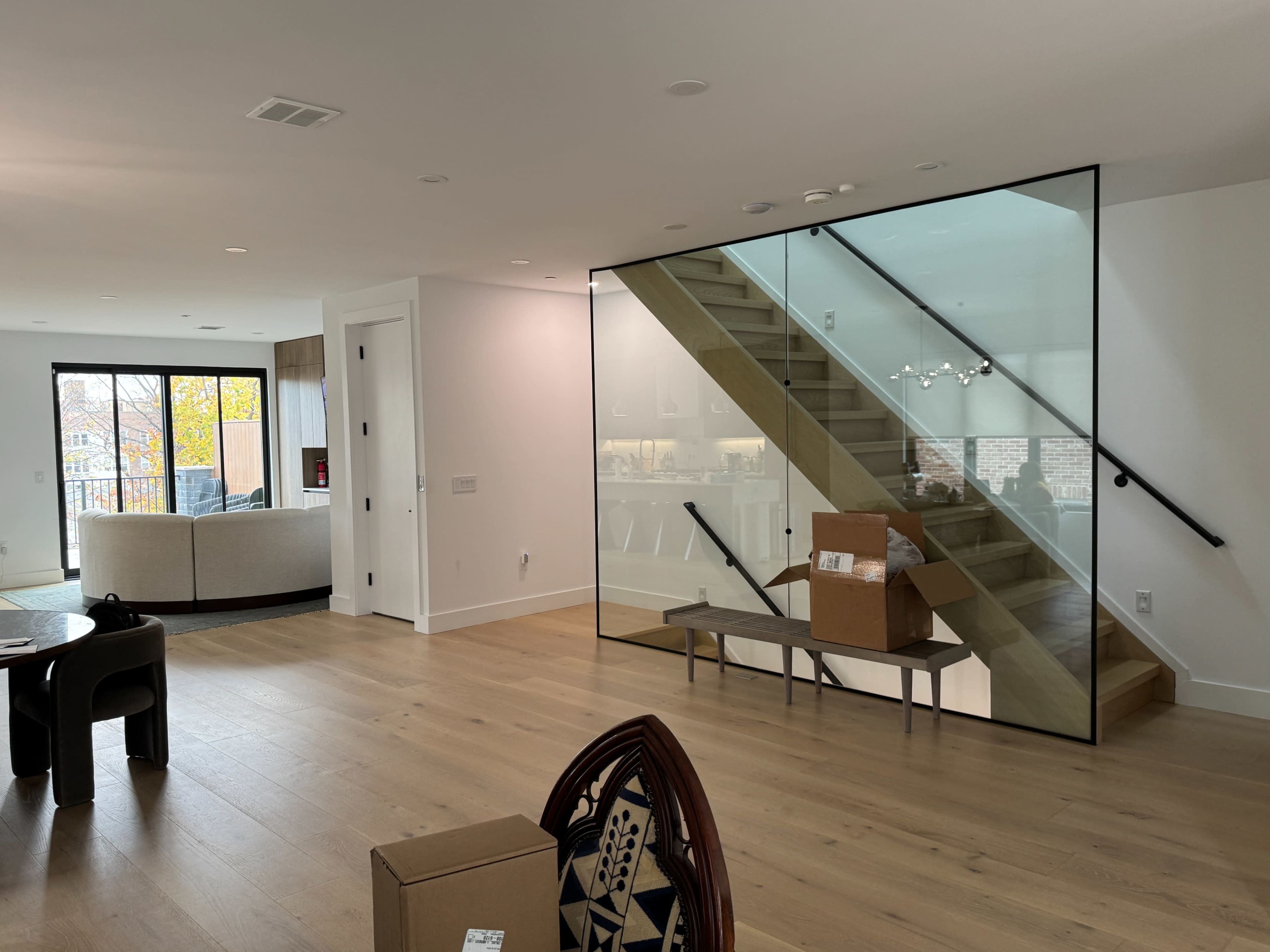 The image features a modern interior space with a glass wall enclosing a staircase, leading to an upper level, and visible light-colored wood flooring throughout.