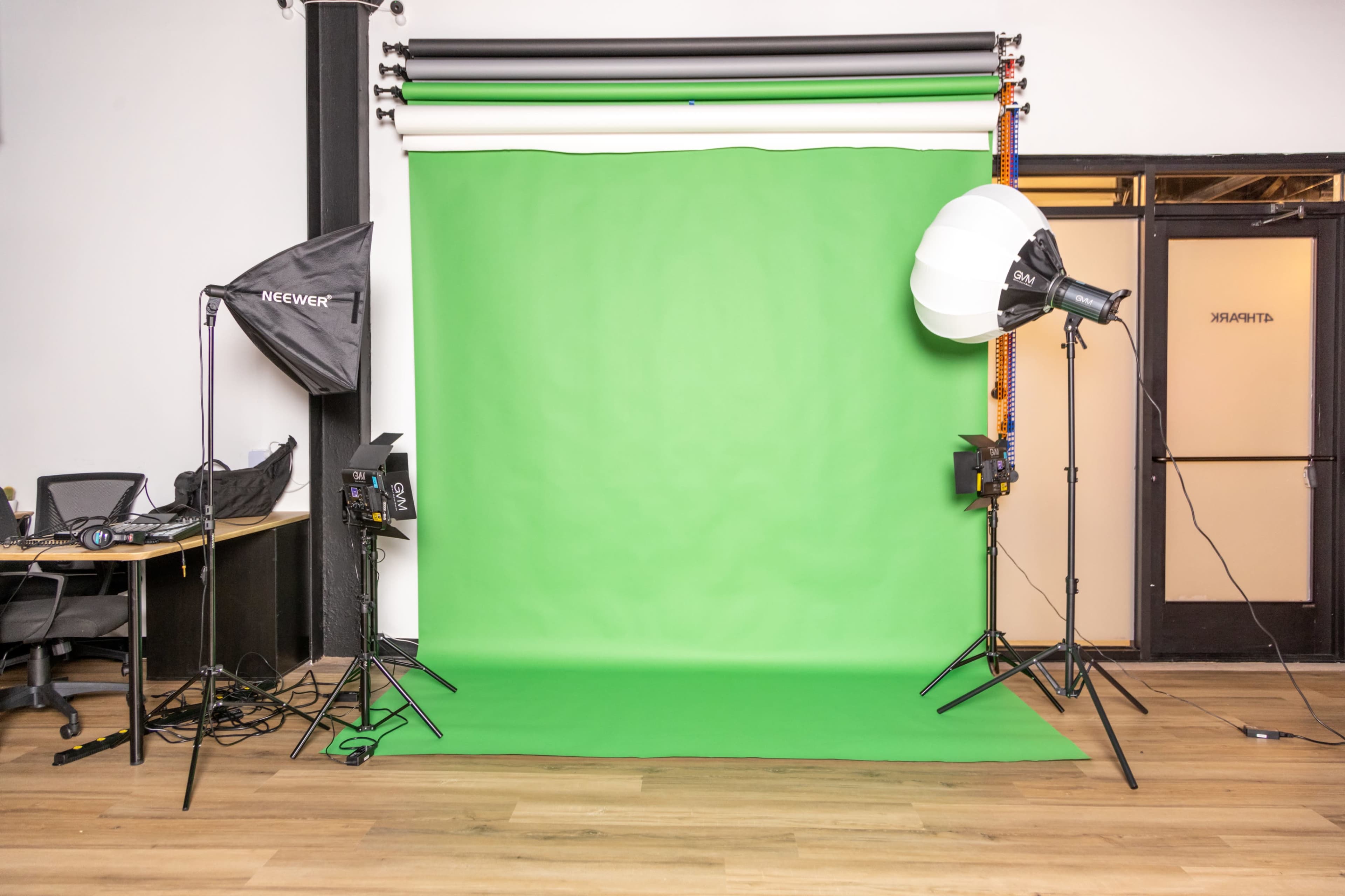 A photo studio setup with a green backdrop, lighting equipment, and an empty work area in the background.