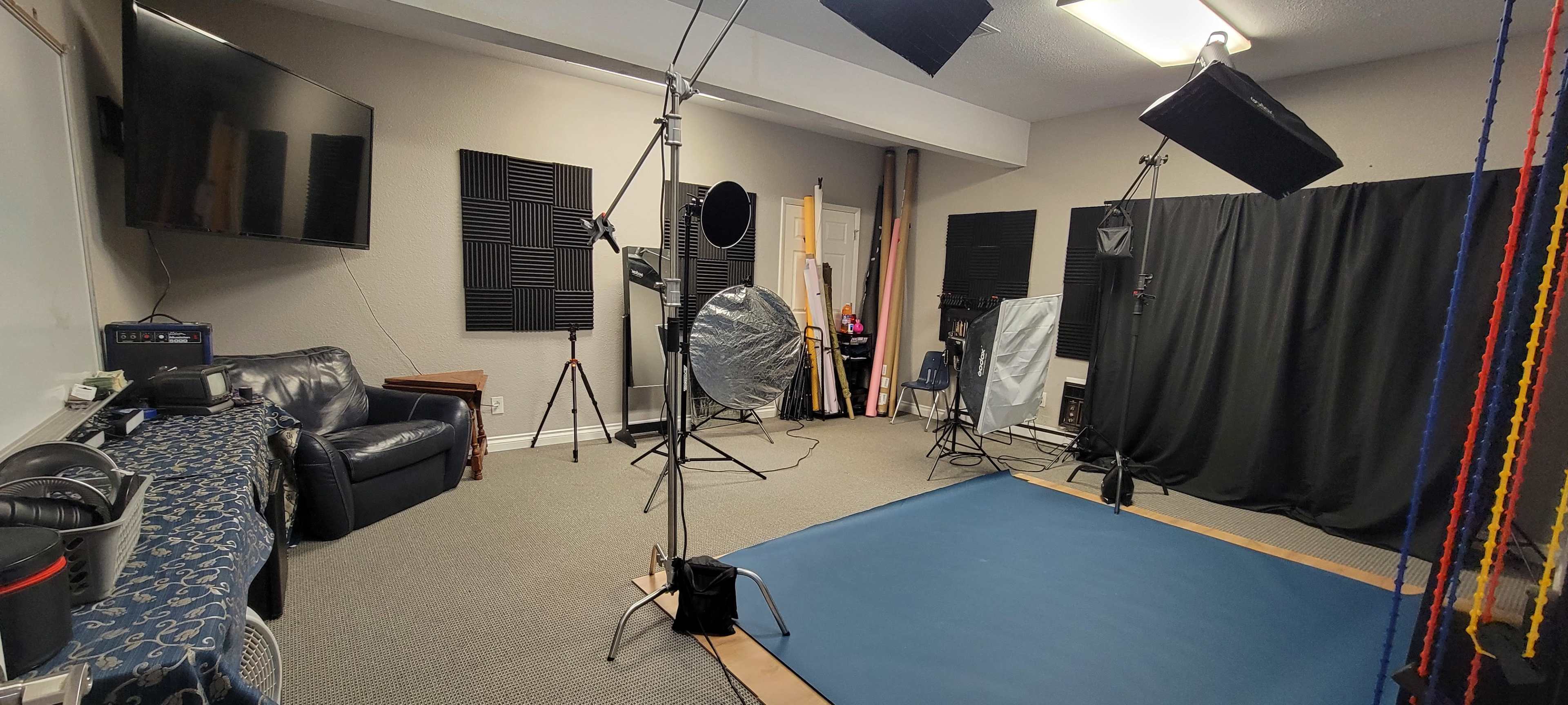 A photography studio equipped with lighting gear, a blue backdrop, and soundproofing panels on the walls.