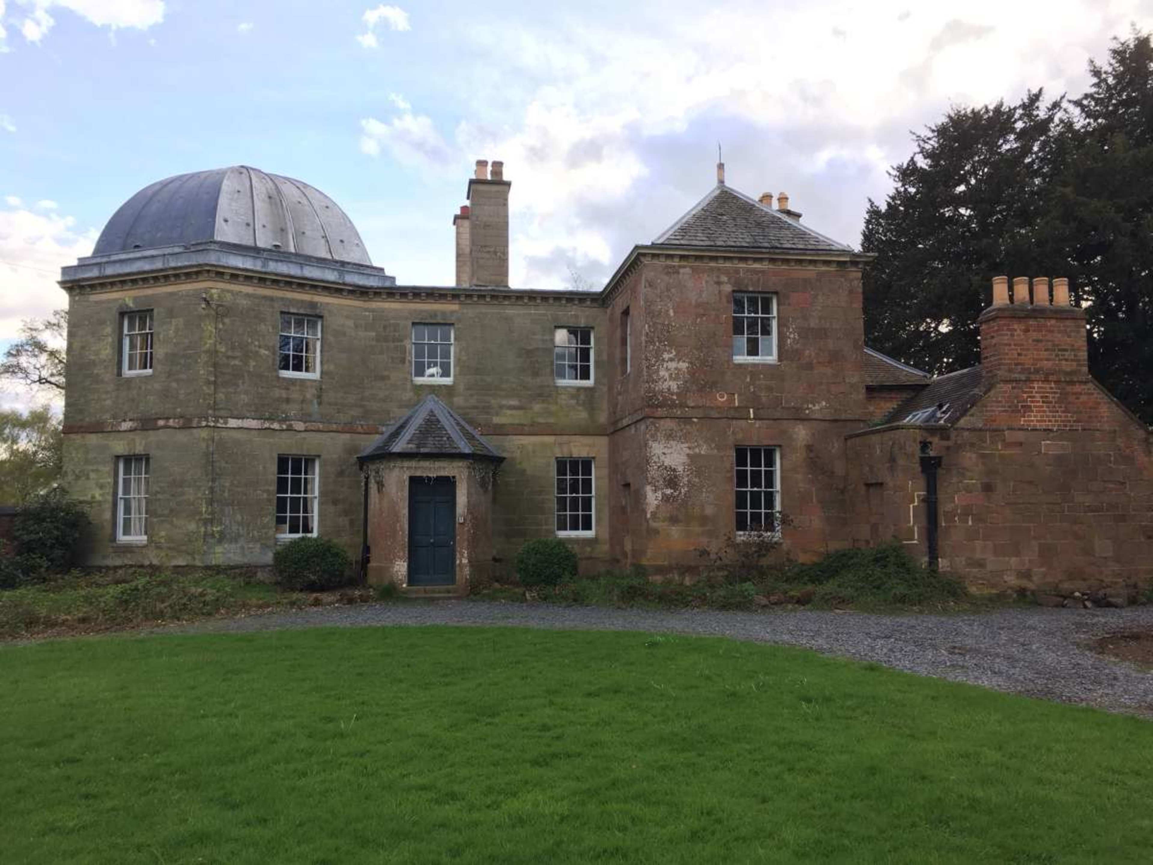 A classical-style house with a dome-shaped roof and multiple chimneys, surrounded by a grassy area.