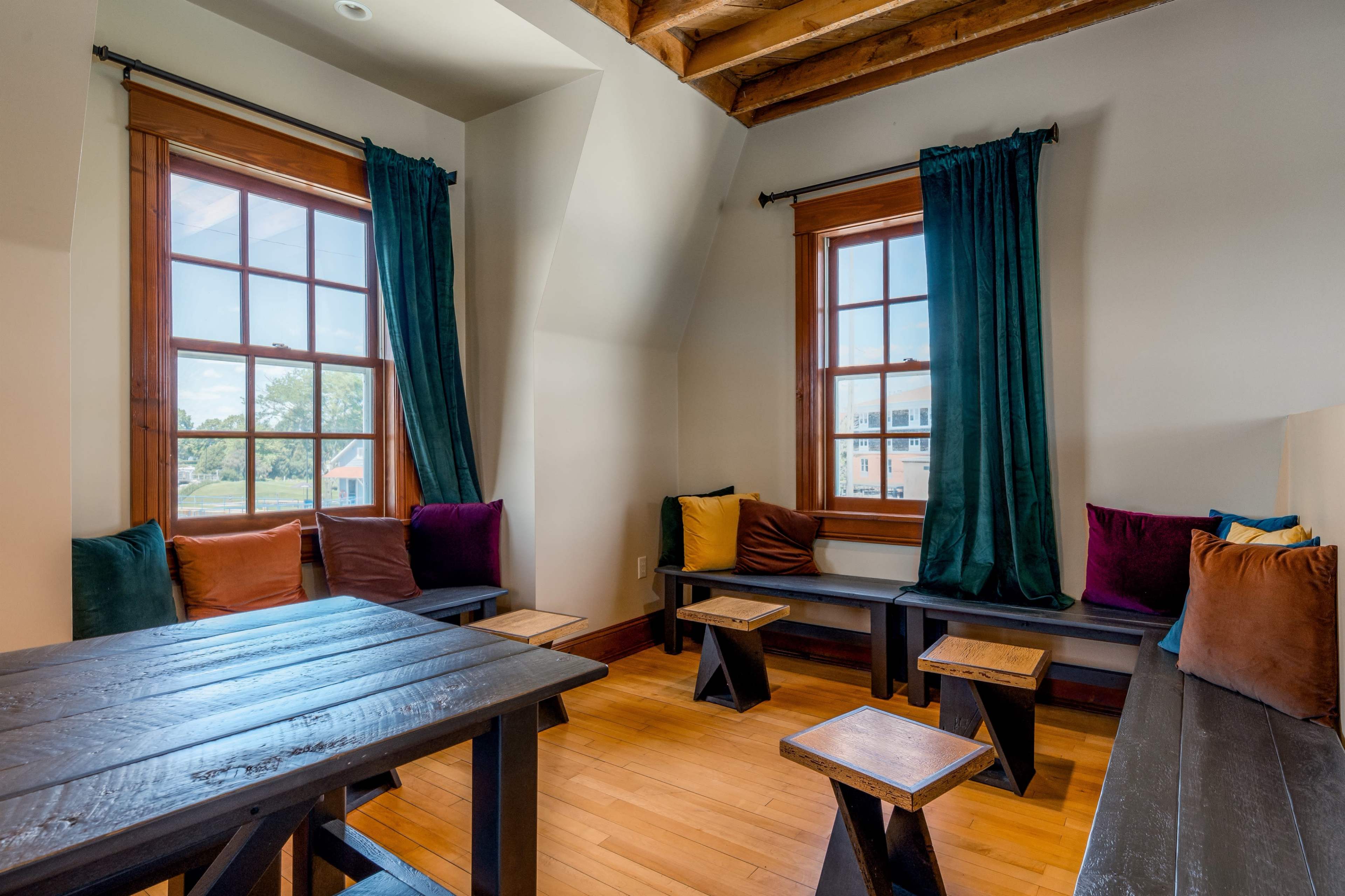 A cozy seating area with two windows, wooden benches, a table, and colorful cushions.