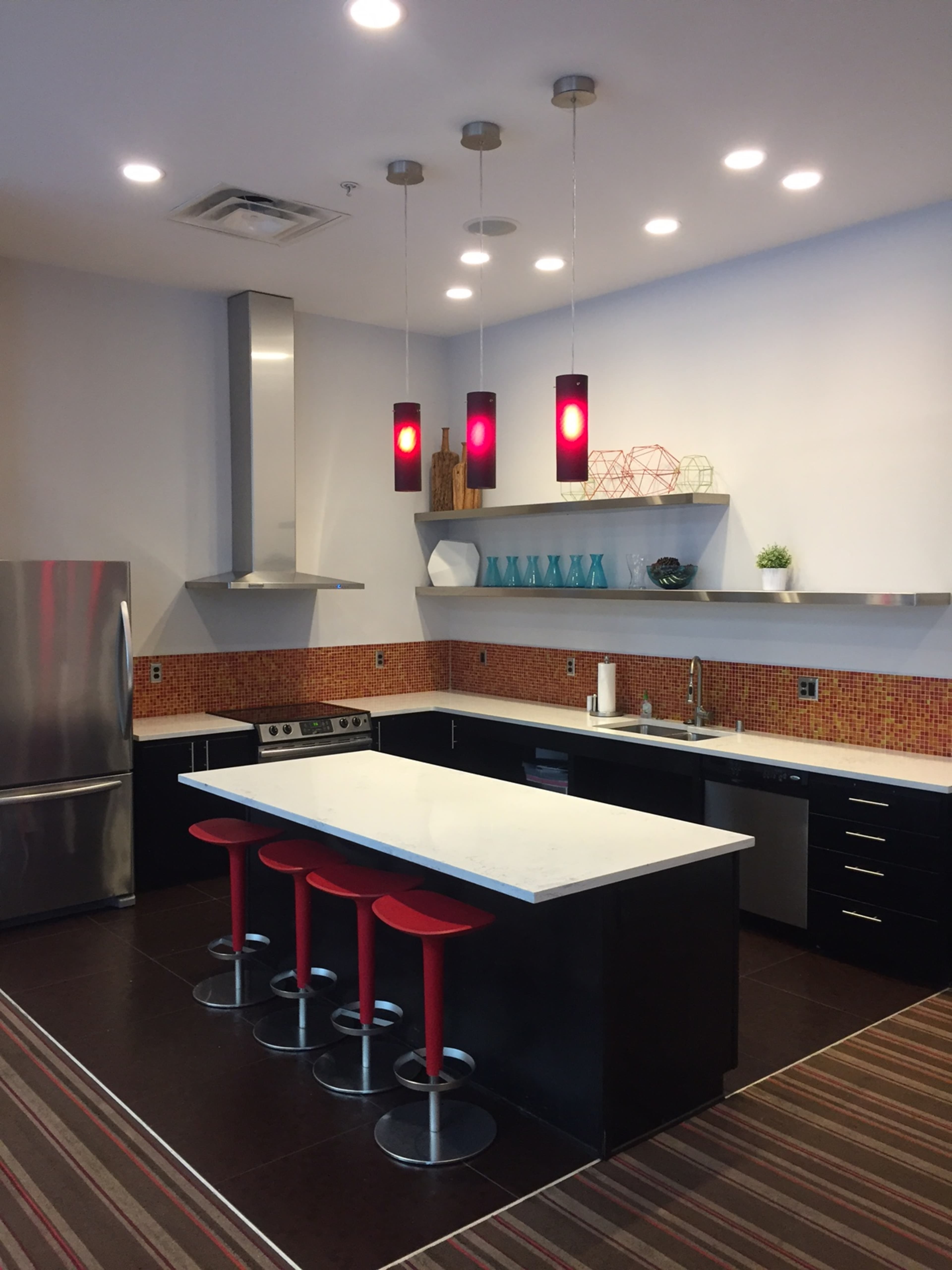A modern kitchen with a large island featuring red stools, stainless steel appliances, and a colorful mosaic backsplash.