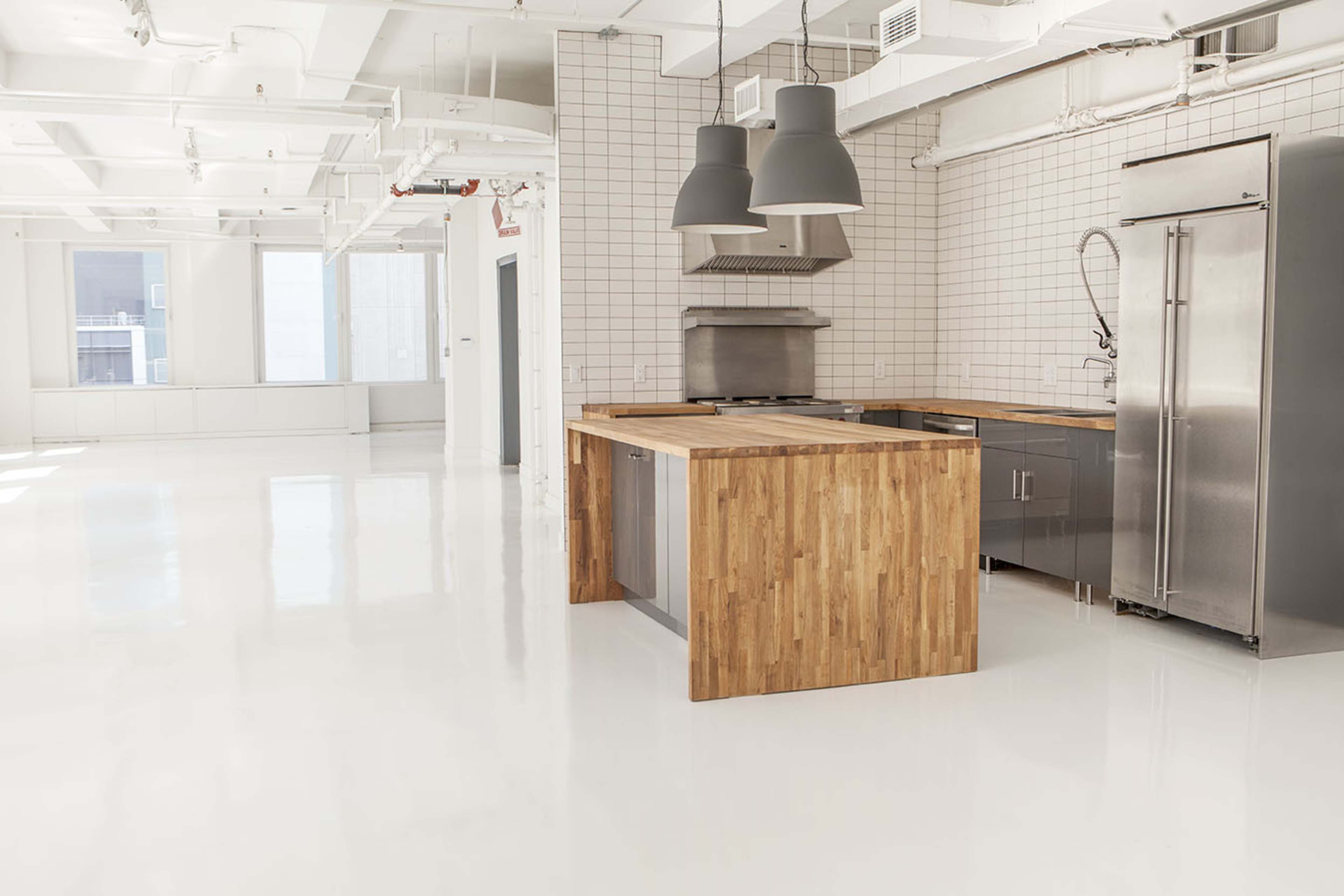 A modern kitchen with a wooden island, stainless steel appliances, and a tiled backsplash in a spacious, bright room.