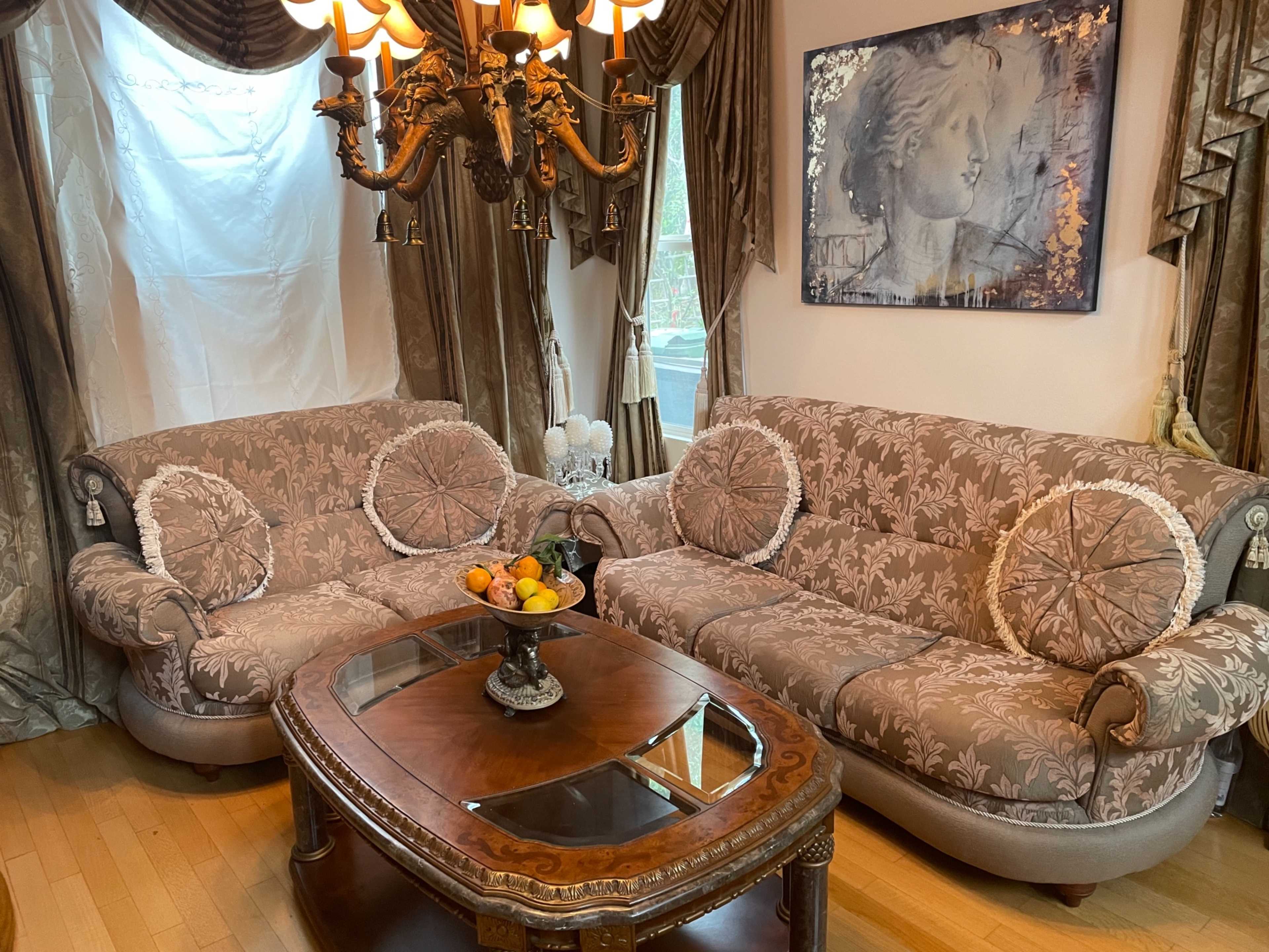 A living room with two patterned sofas, a wooden coffee table with a fruit bowl, and a chandelier hanging above.