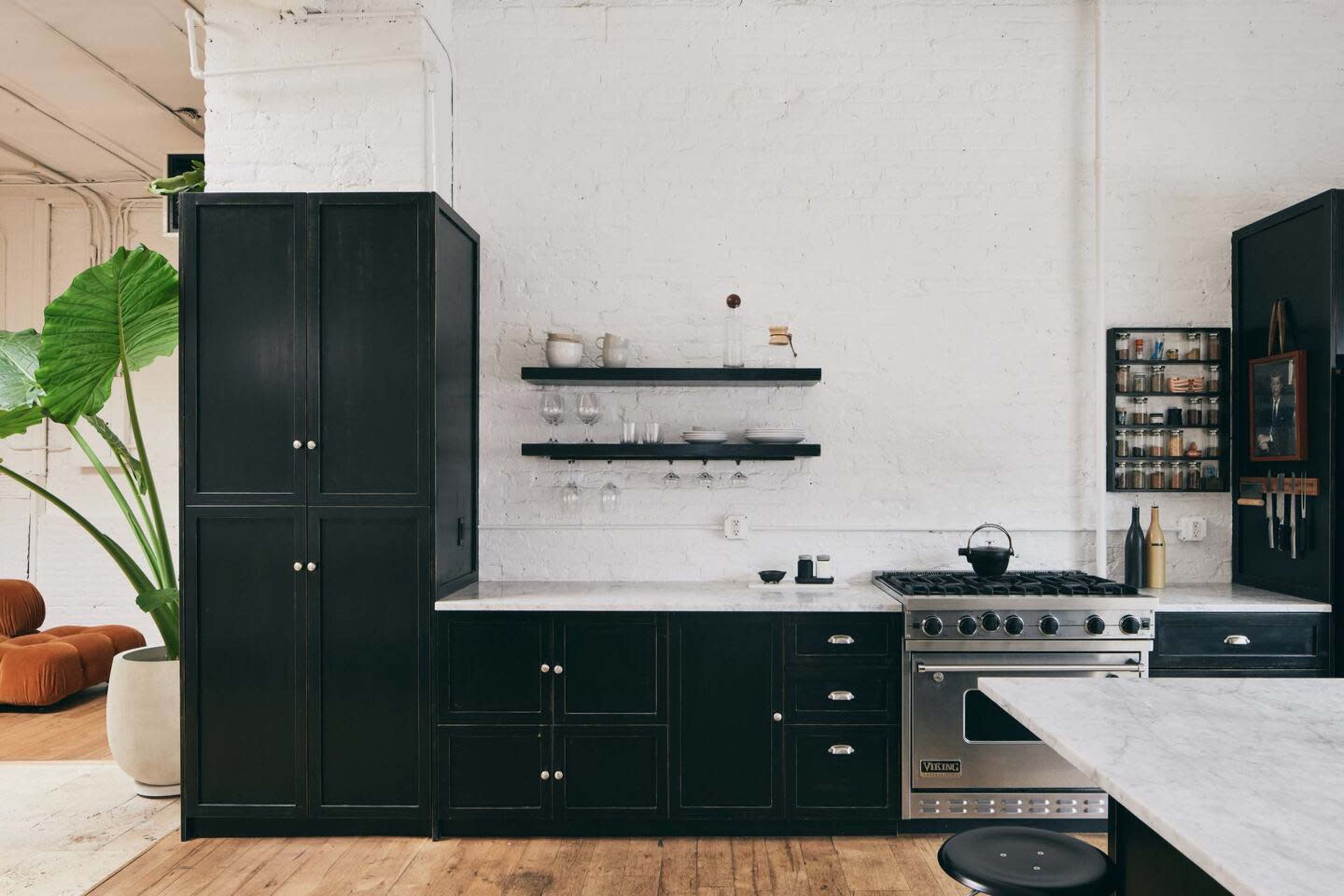 A modern kitchen features black cabinetry, a stainless steel stove, and open shelving against a white brick wall.