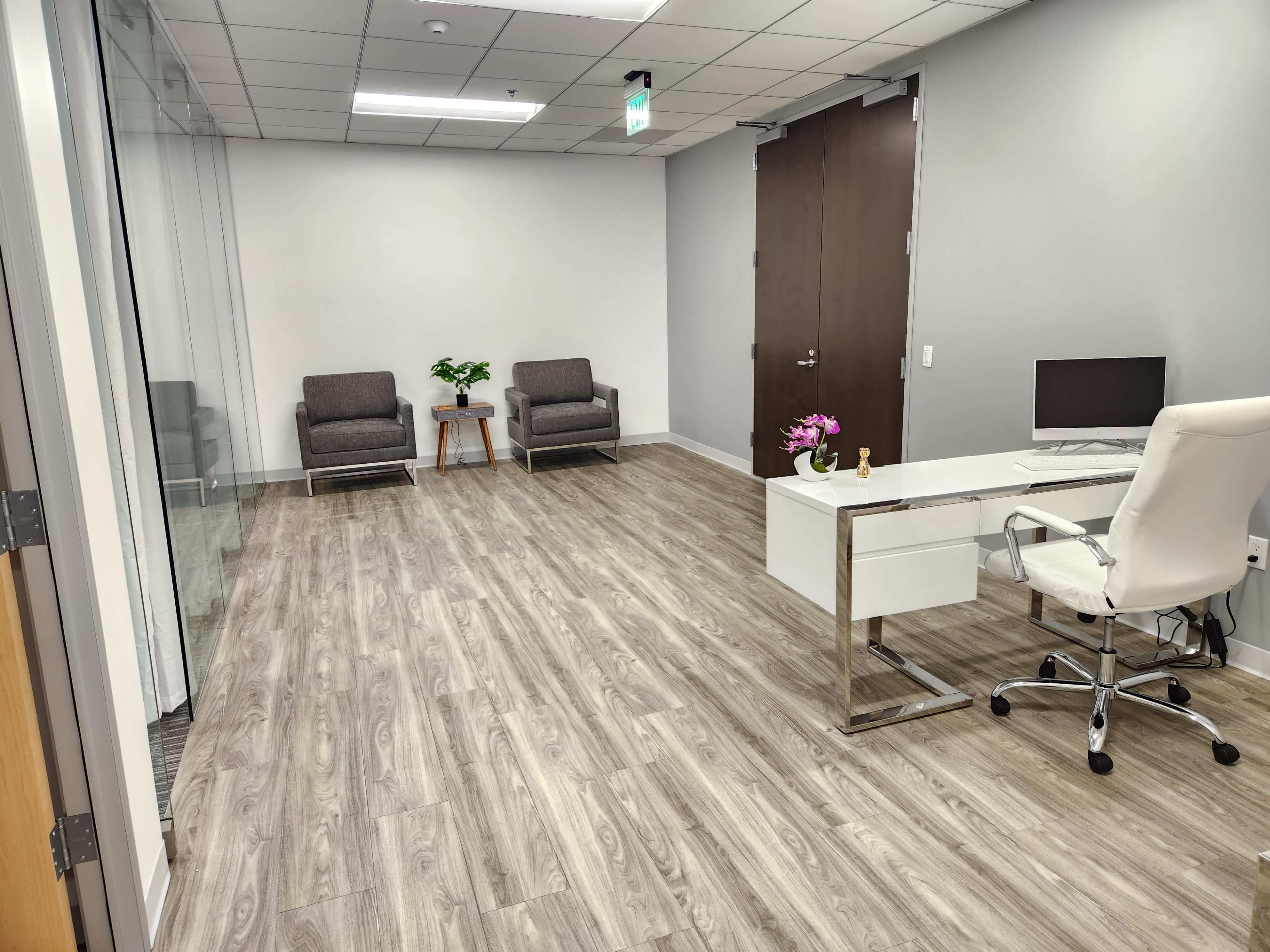 A modern office space with two chairs, a desk with a computer, and wood-like flooring.