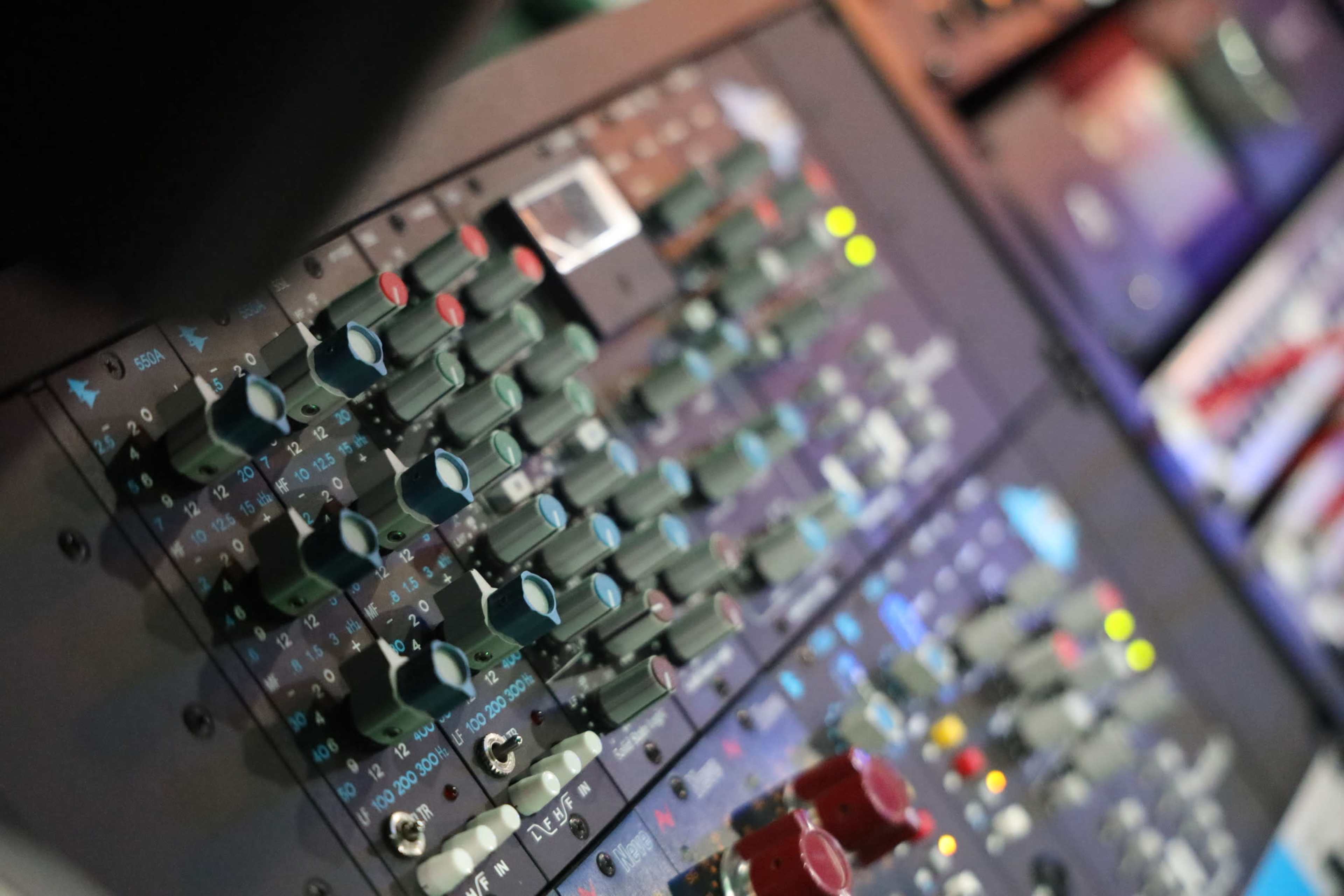 A close-up of a sound mixing console with various knobs, sliders, and lights arranged in a grid pattern.
