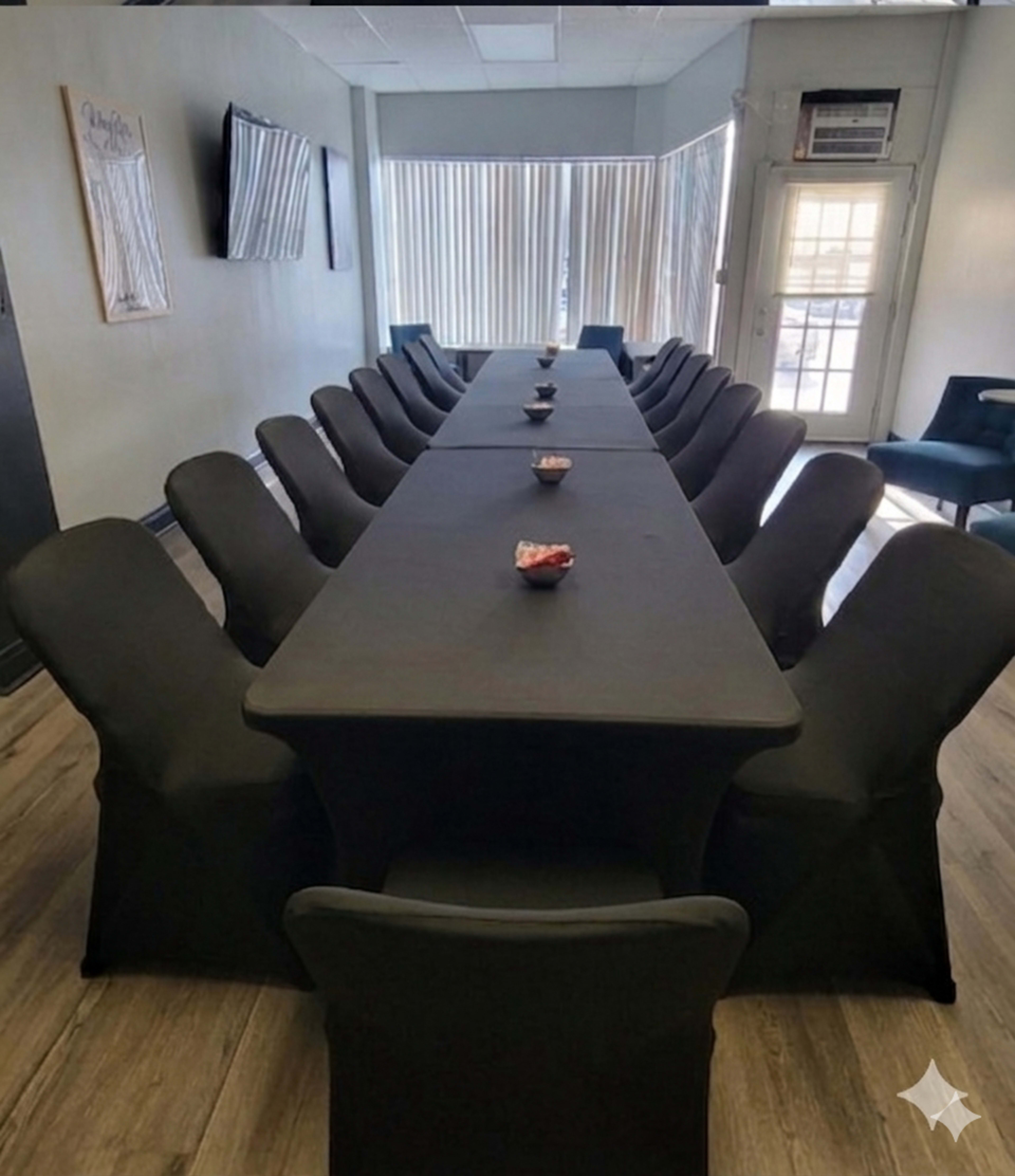 A long black table is set for a meeting, surrounded by sleek black chairs, with small bowls at intervals along the table.