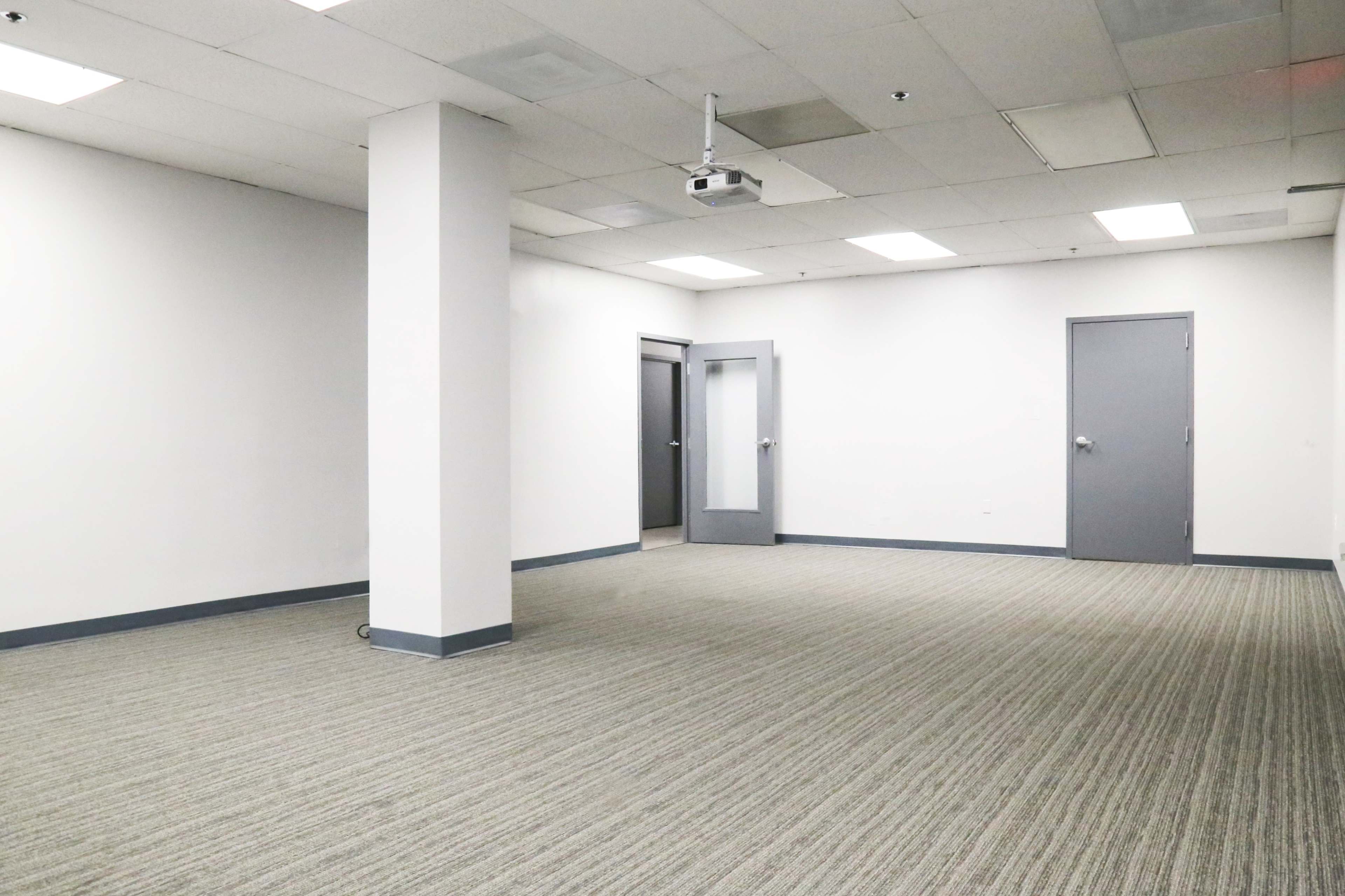 An empty room with gray carpet, white walls, and a door with a glass panel on one side.