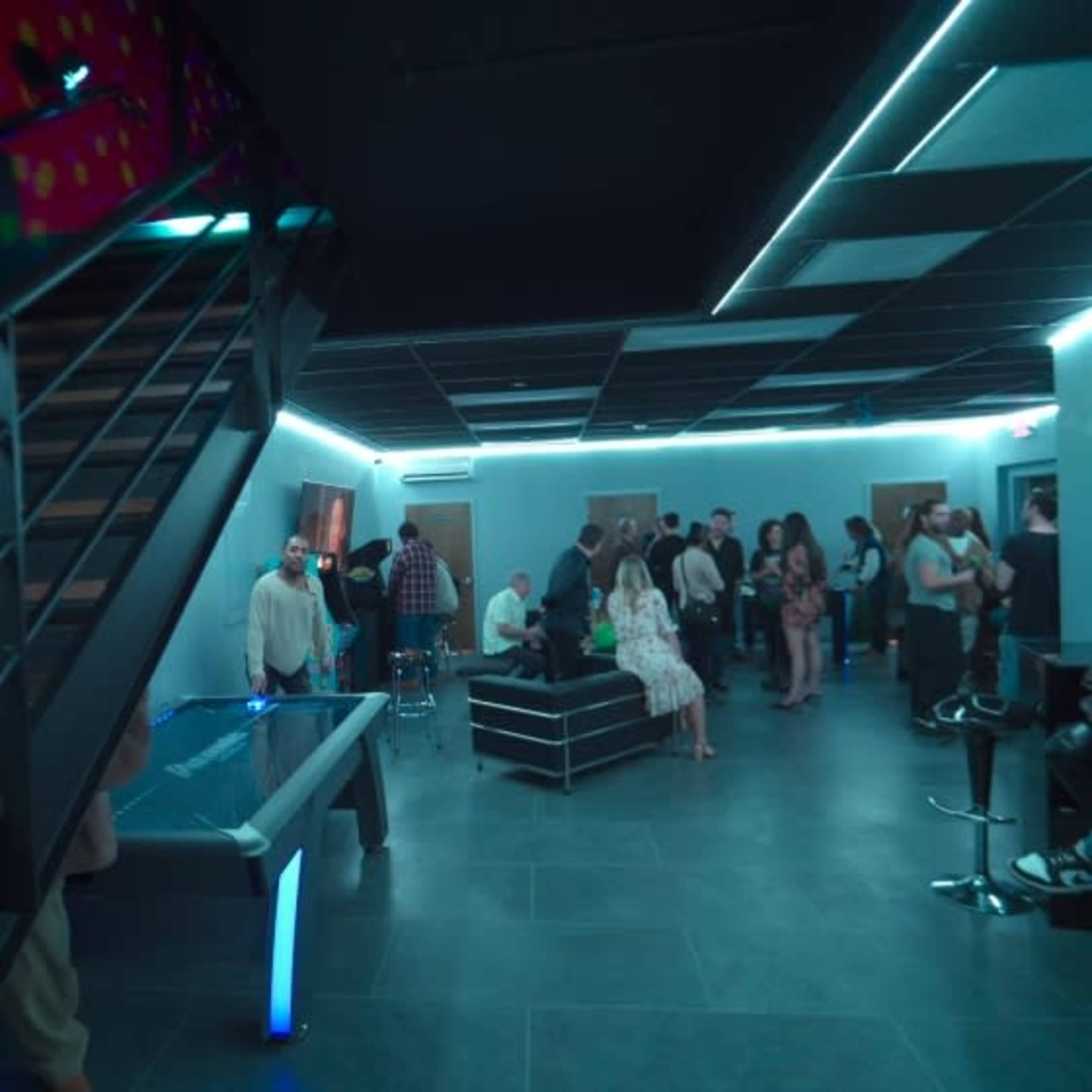 The image shows a modern lounge area with people socializing, a pool table, and illuminated blue lighting.