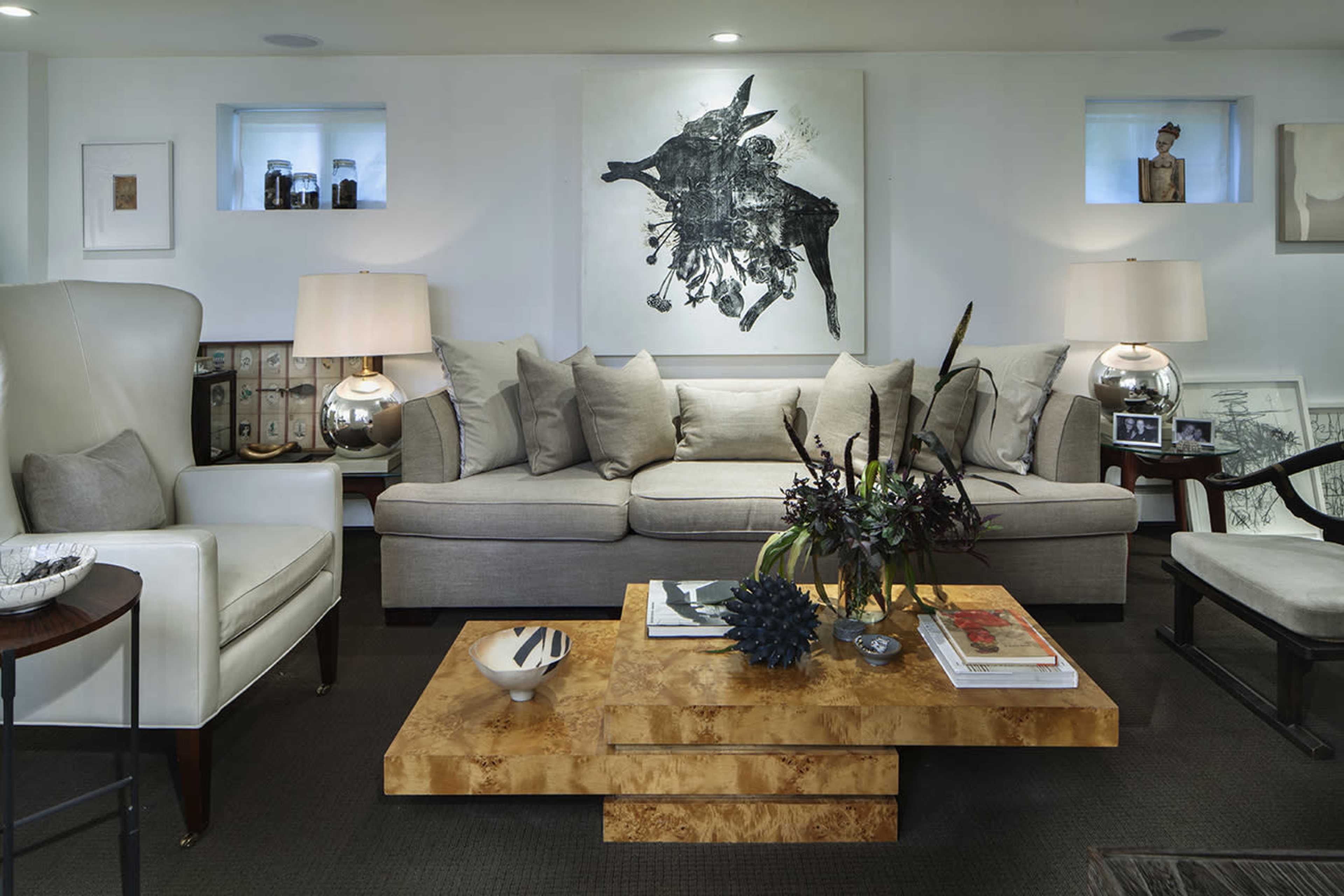 The image depicts a modern living room featuring a light-colored sofa with cushions, a coffee table with a unique design, and artwork on the walls, accompanied by decorative lamps and various decorative items.