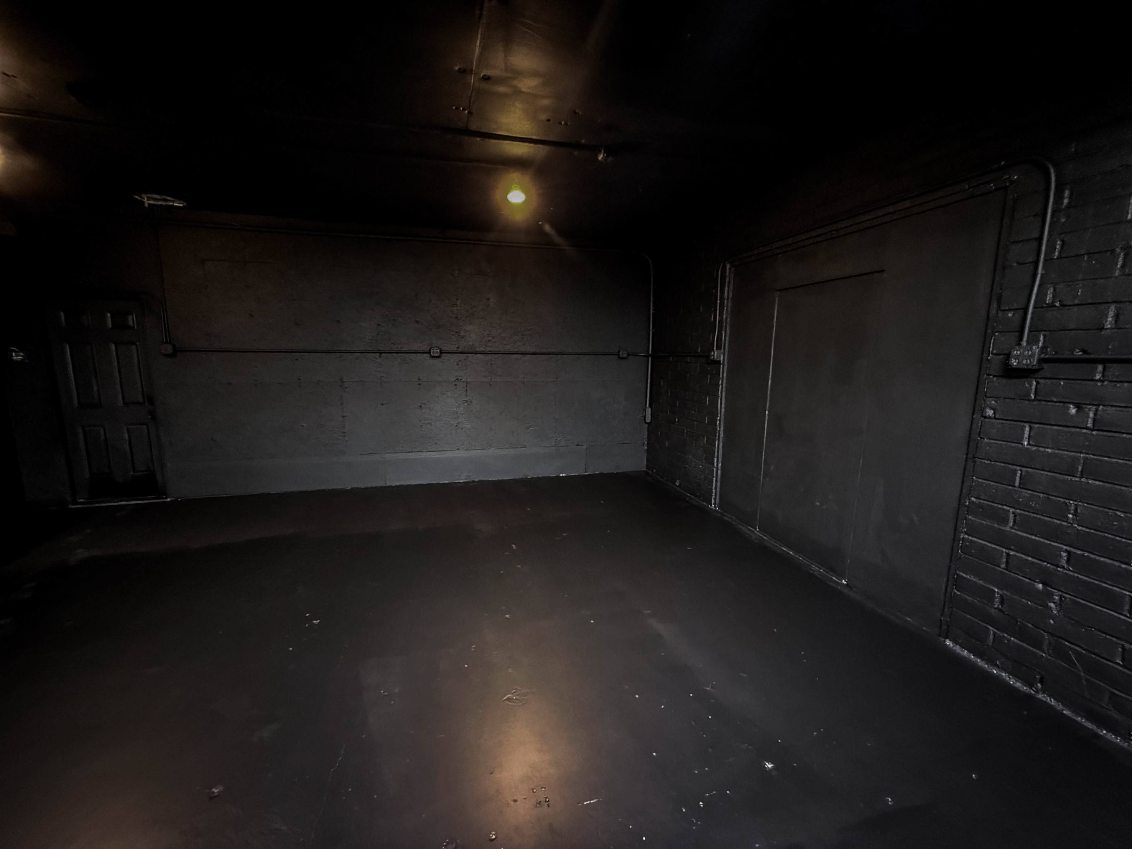 The image shows a dimly lit, empty room with dark walls and a smooth floor.