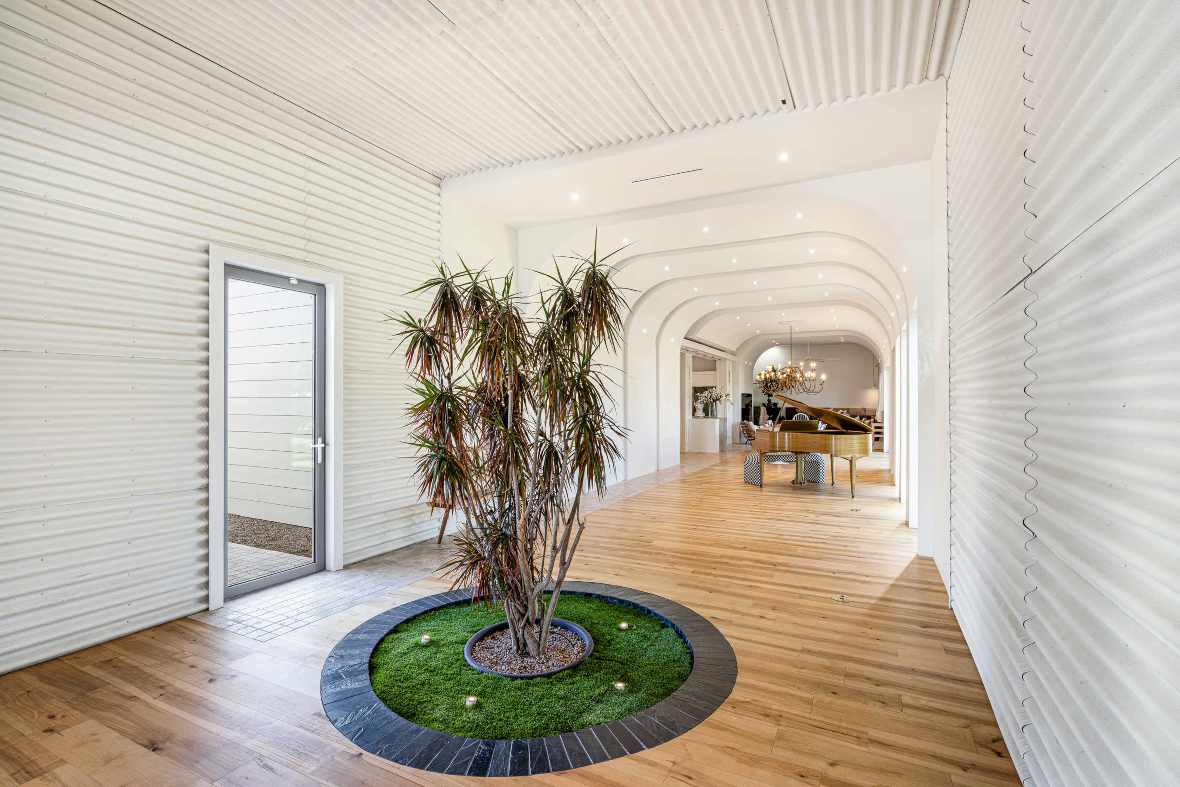 A hallway features a central potted plant surrounded by a circular stone base, leading to an arched entrance that opens into a spacious area with wooden flooring.