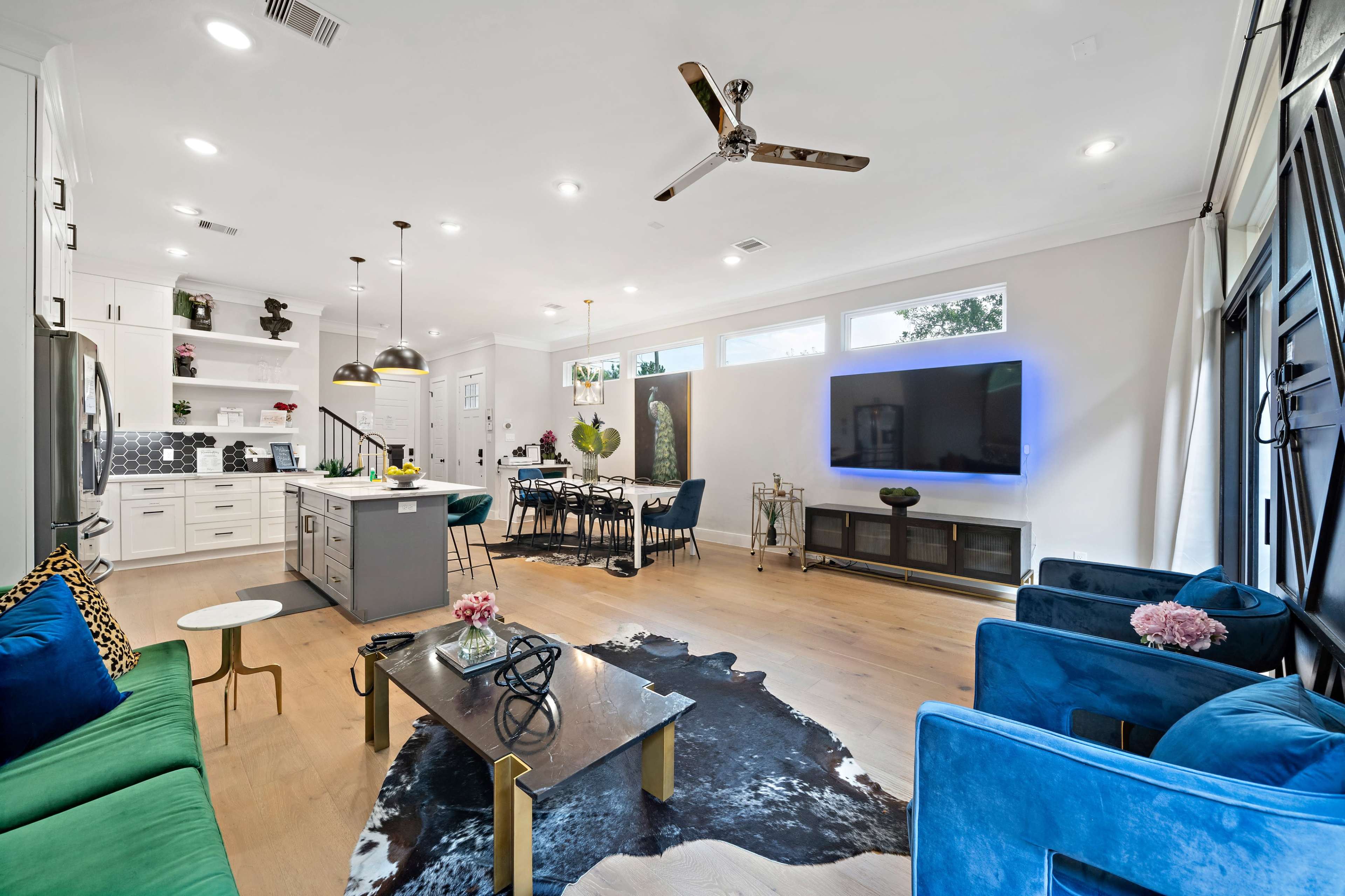 A modern living room and dining area with a kitchen island, a large television, and a mix of seating arrangements.