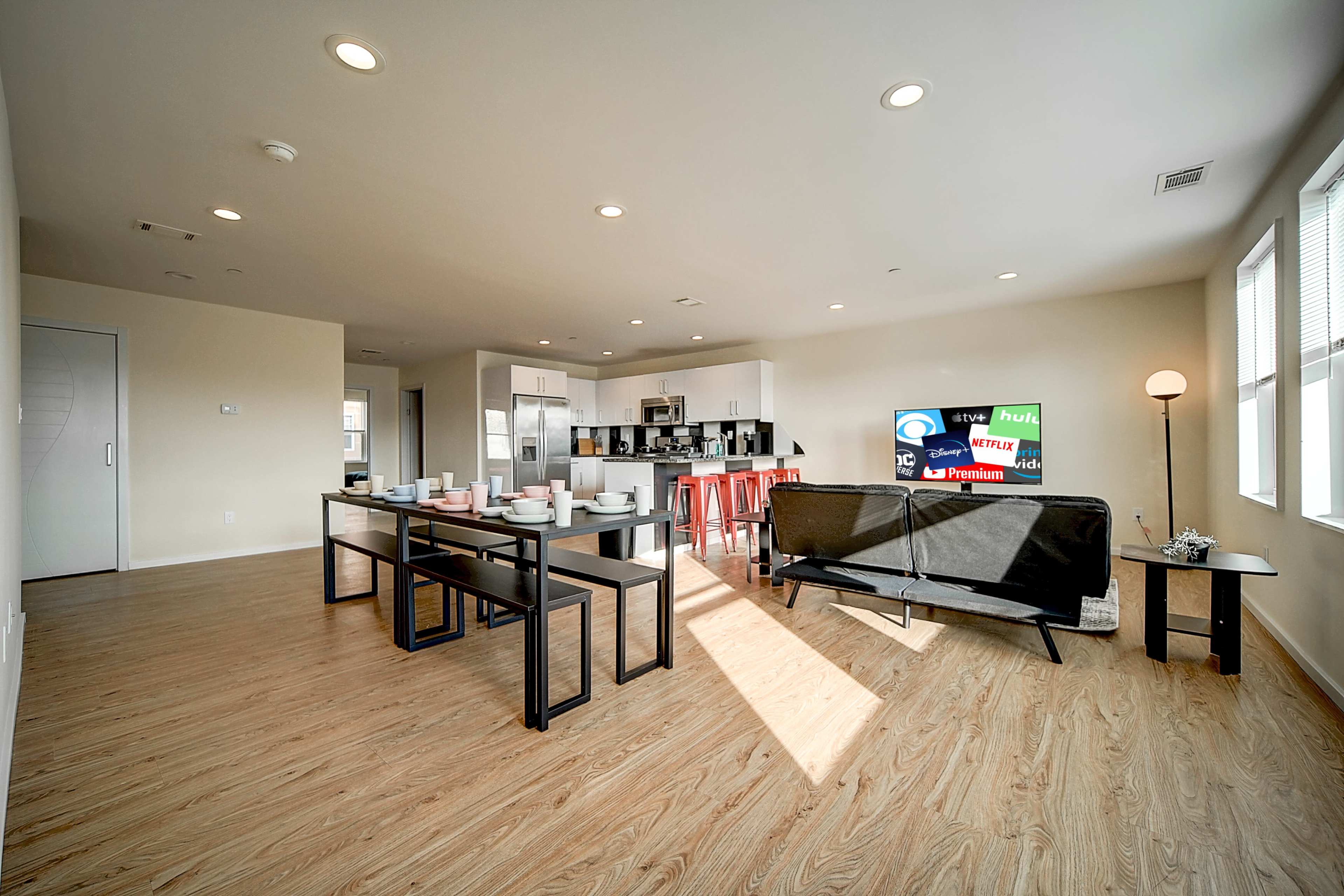 A modern open-concept living area with a dining table set for several people, a couch, and a kitchen in the background.