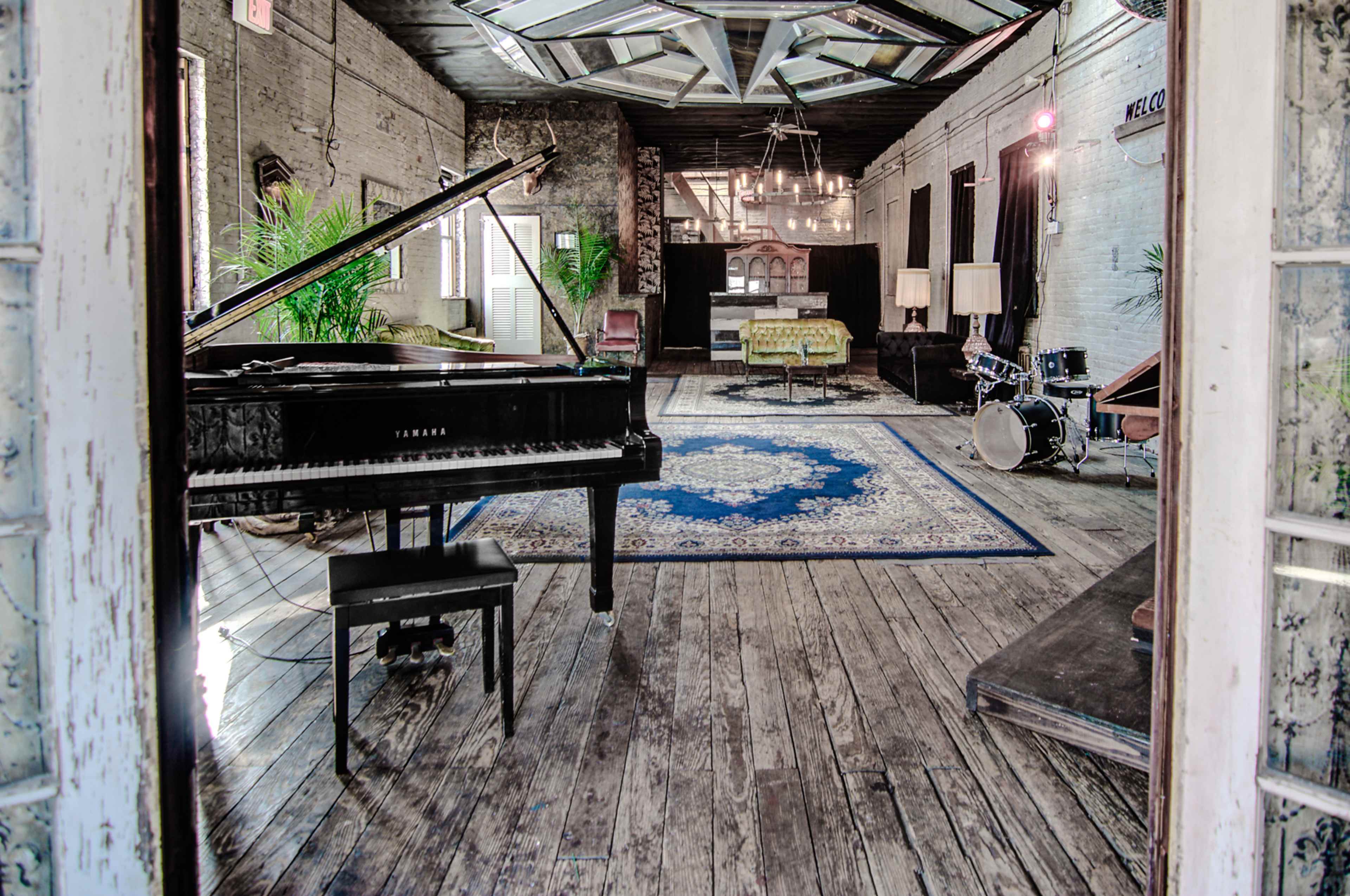 A spacious room with a grand piano, a drum set, and various seating areas on a wooden floor.