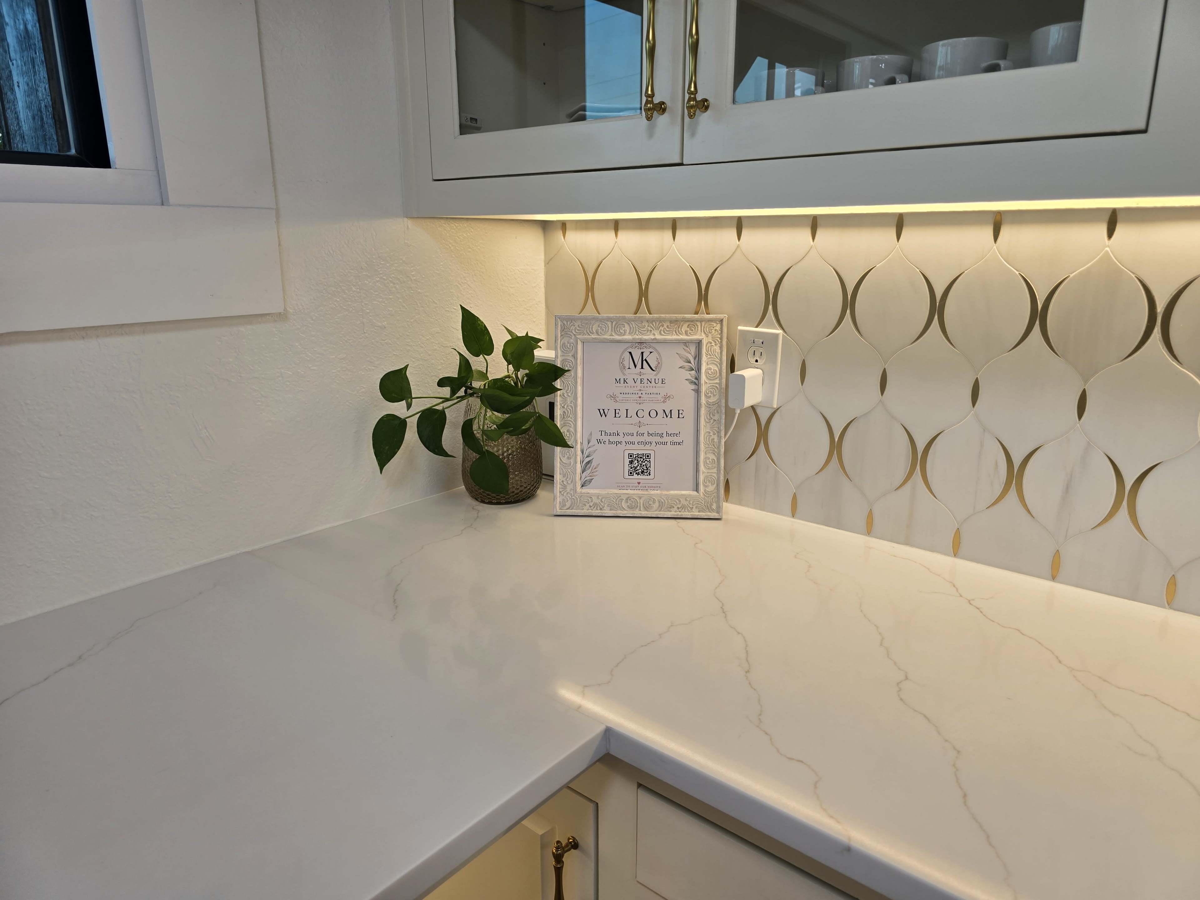 A countertop with a decorative sign that says "WELCOME" and a small potted plant next to it, set against a background of gold-accented wall panels and cabinetry.