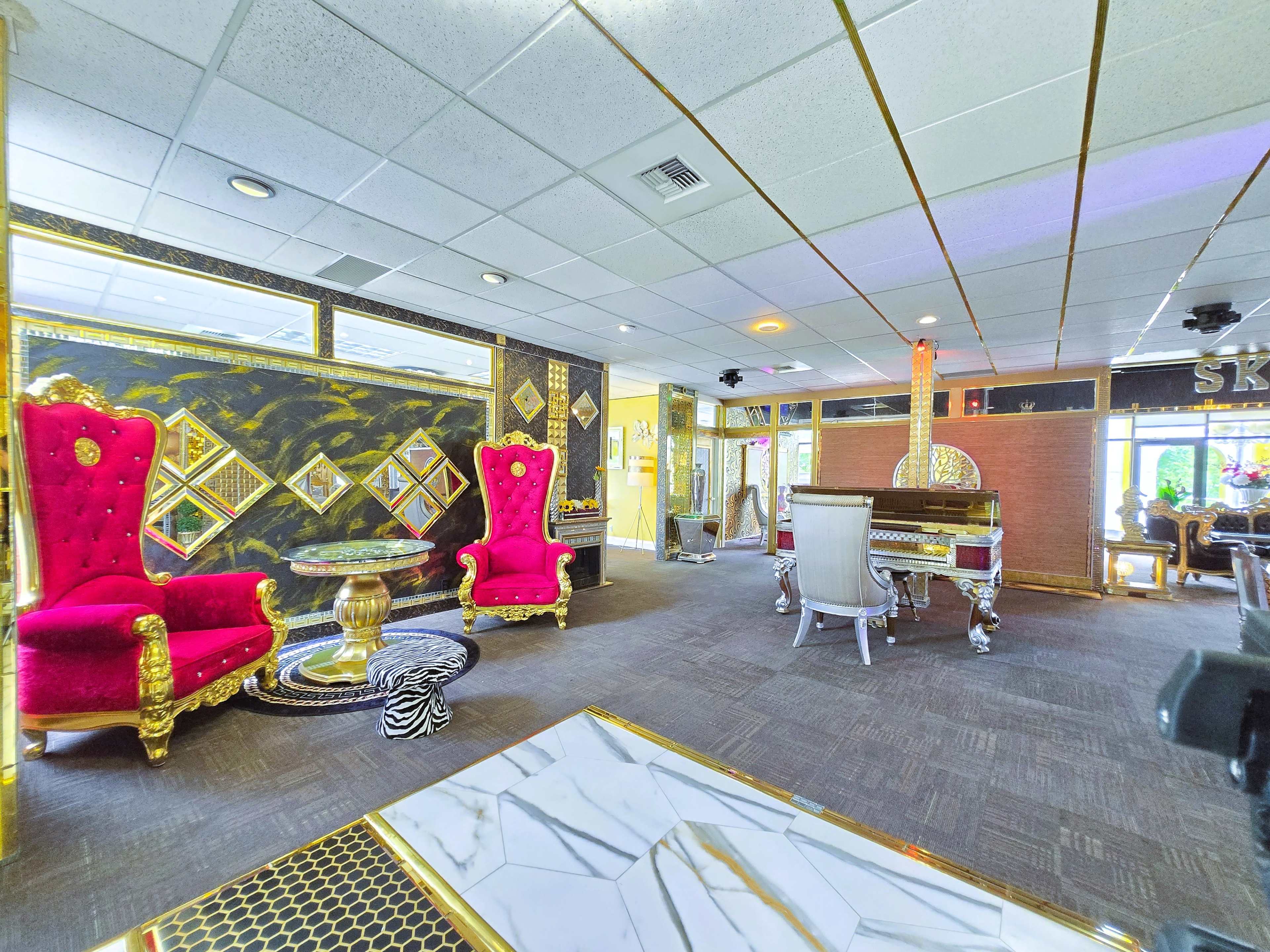 The image shows a lavish interior space featuring two red velvet chairs with gold accents, a grand piano, and ornate decor throughout.