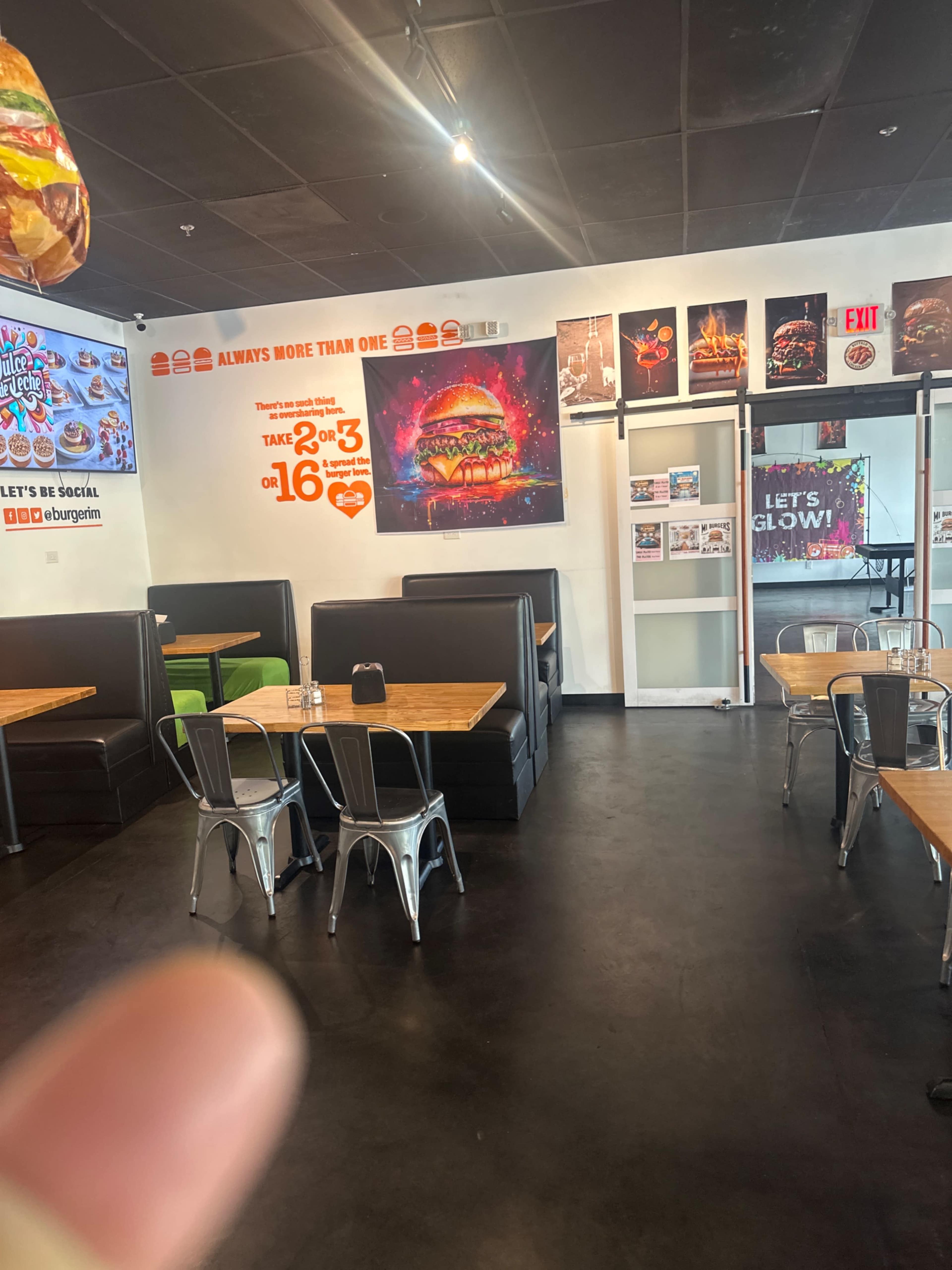The image shows the interior of a casual dining restaurant featuring black booths, wooden tables, and burger-themed wall art.